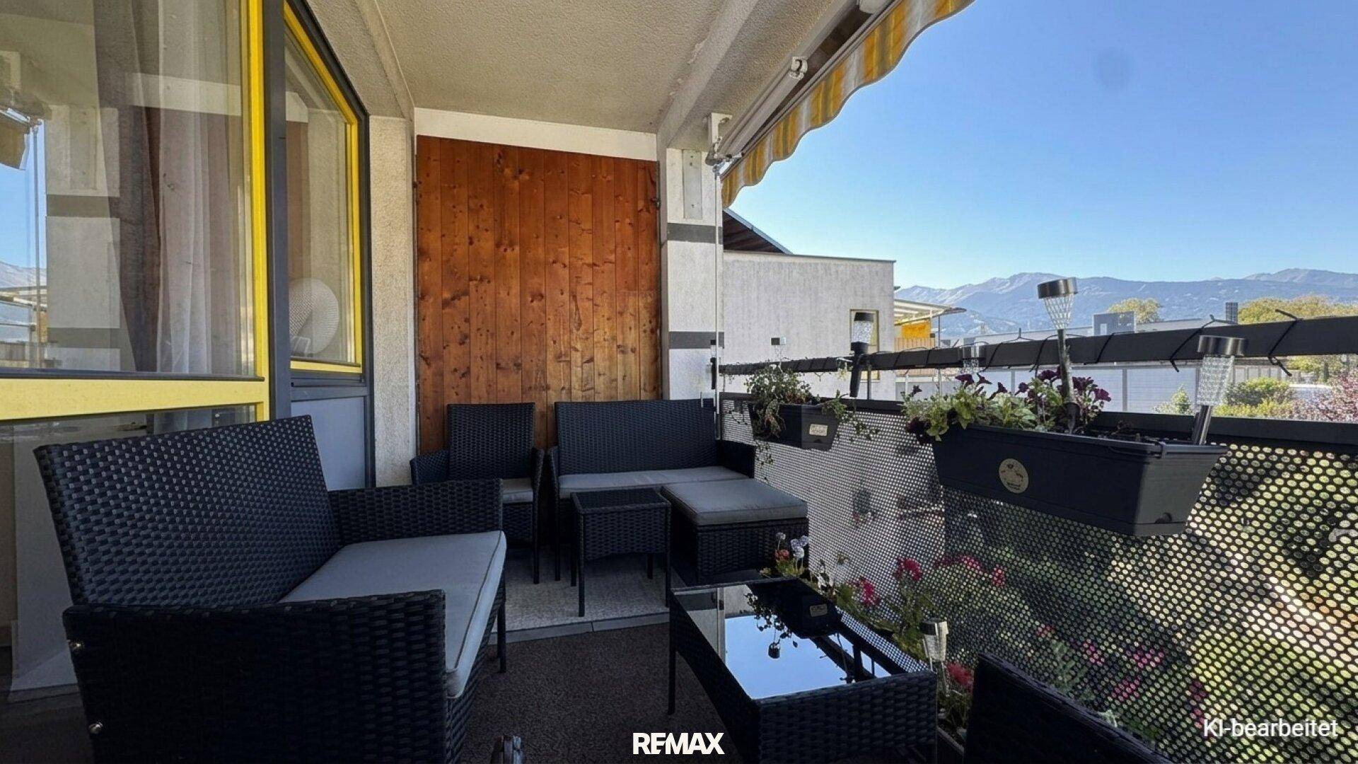 Möblierter Balkon mit Rattan-Sitzgruppe und Fernblick auf die Berge.