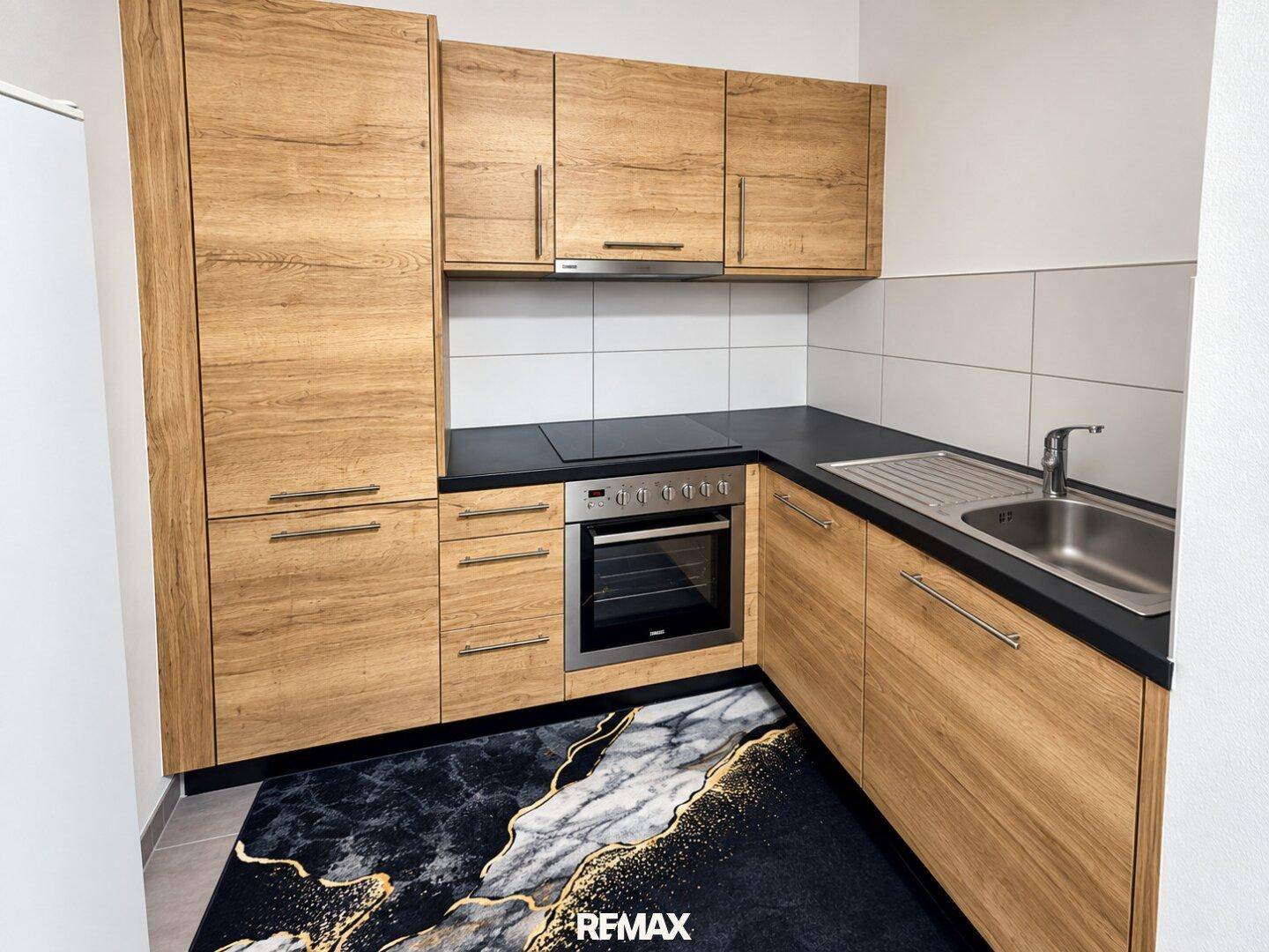 Funktionale Küche mit Holzoptik-Schränken, schwarzer Arbeitsplatte und integrierten Elektrogeräten.