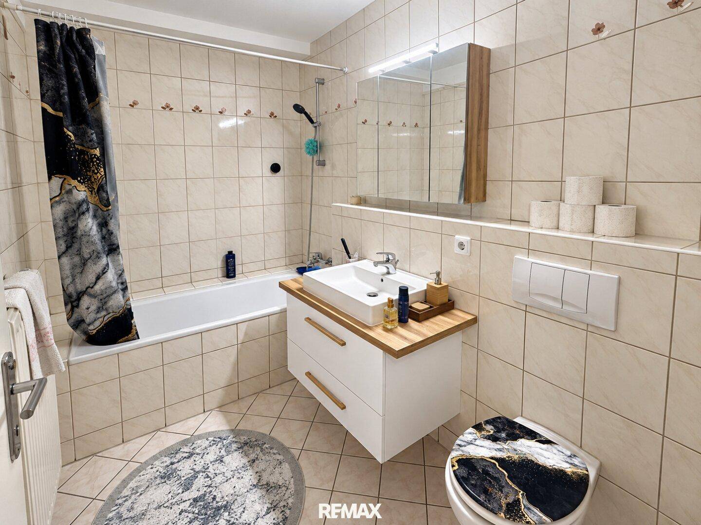Gefliestes Badezimmer mit Badewanne, Waschbeckenunterschrank und Spiegelschrank.