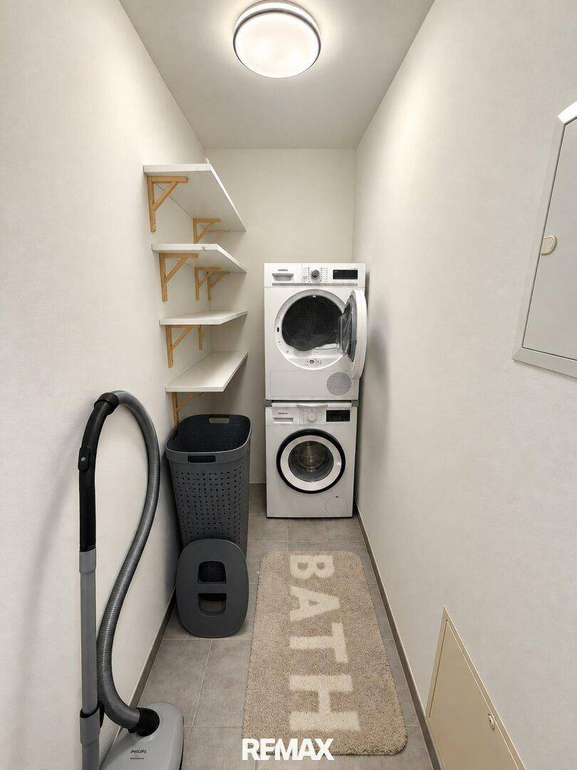 Praktischer Hauswirtschaftsraum mit Waschmaschine, Trockner und Wandregalen für zusätzlichen Stauraum.