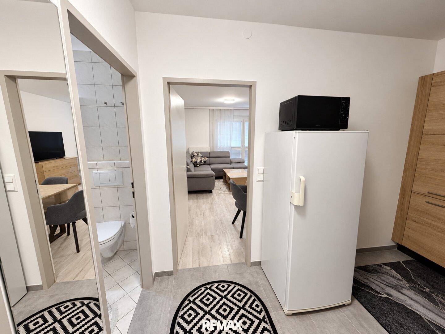 Flur mit Kühlschrank und Durchgang zu weiteren Räumen, inklusive Blick ins Badezimmer.