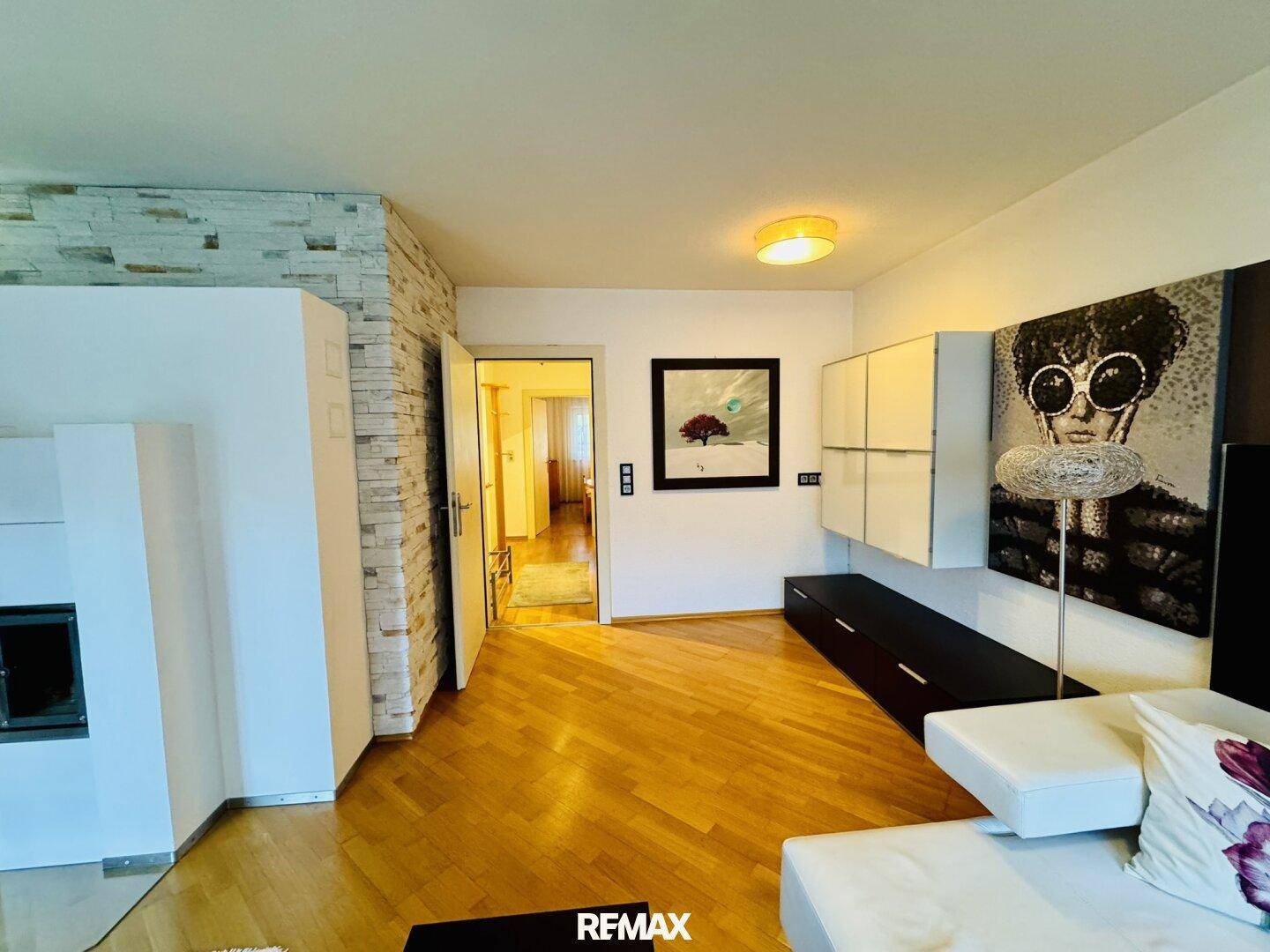 Helles Wohnzimmer mit Holzboden, Steinwand und modernem Medienmöbel sowie Kamin.