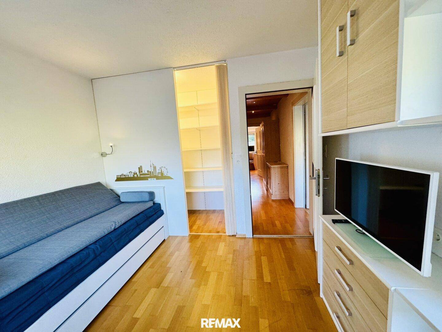 Helles Schlafzimmer mit Holzboden, Schlafsofa und praktischen integrierten Schränken.