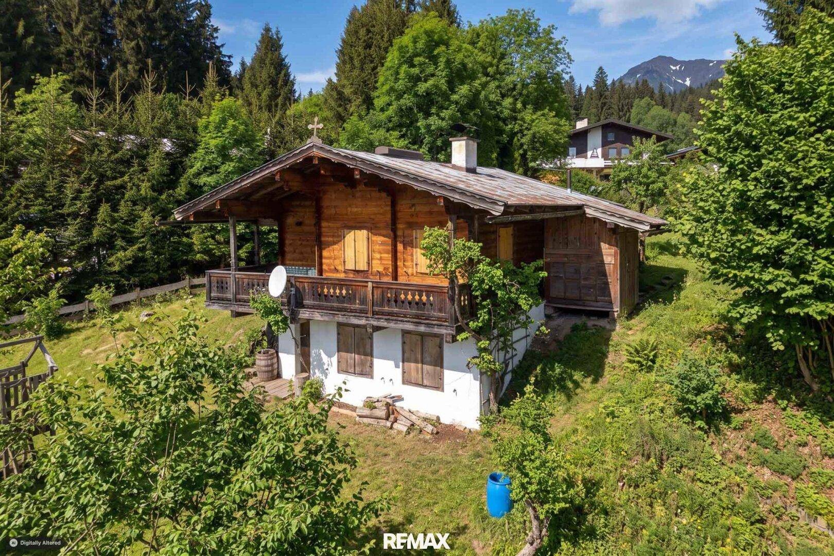 Rustikales Holzchalet mit traditionellem Balkon und weißem Sockelgeschoss, umgeben von üppiger Vegetation.