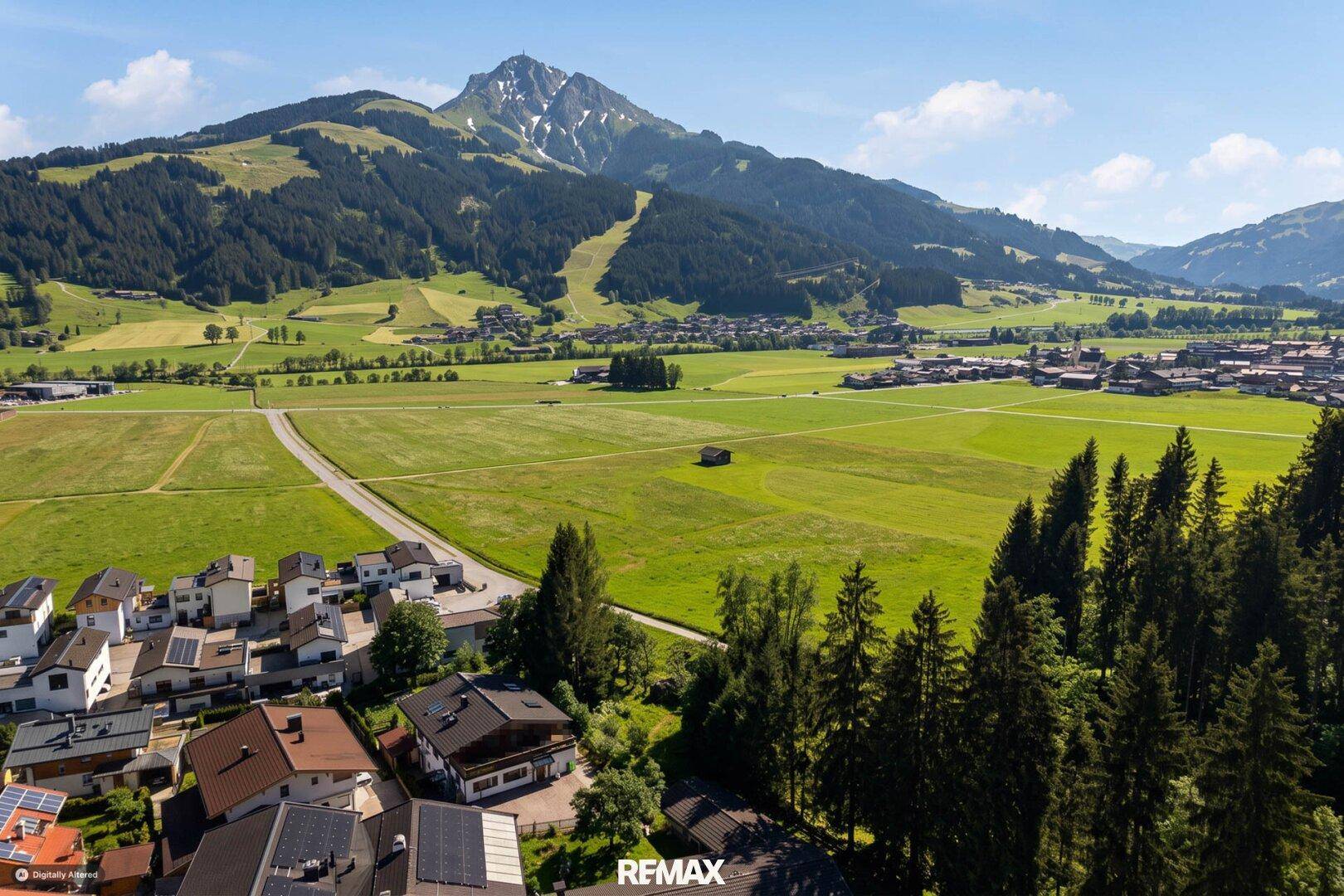 Weitläufige Landschaftsaufnahme mit grünen Feldern, verstreuten Häusern und majestätischem Bergpanorama.