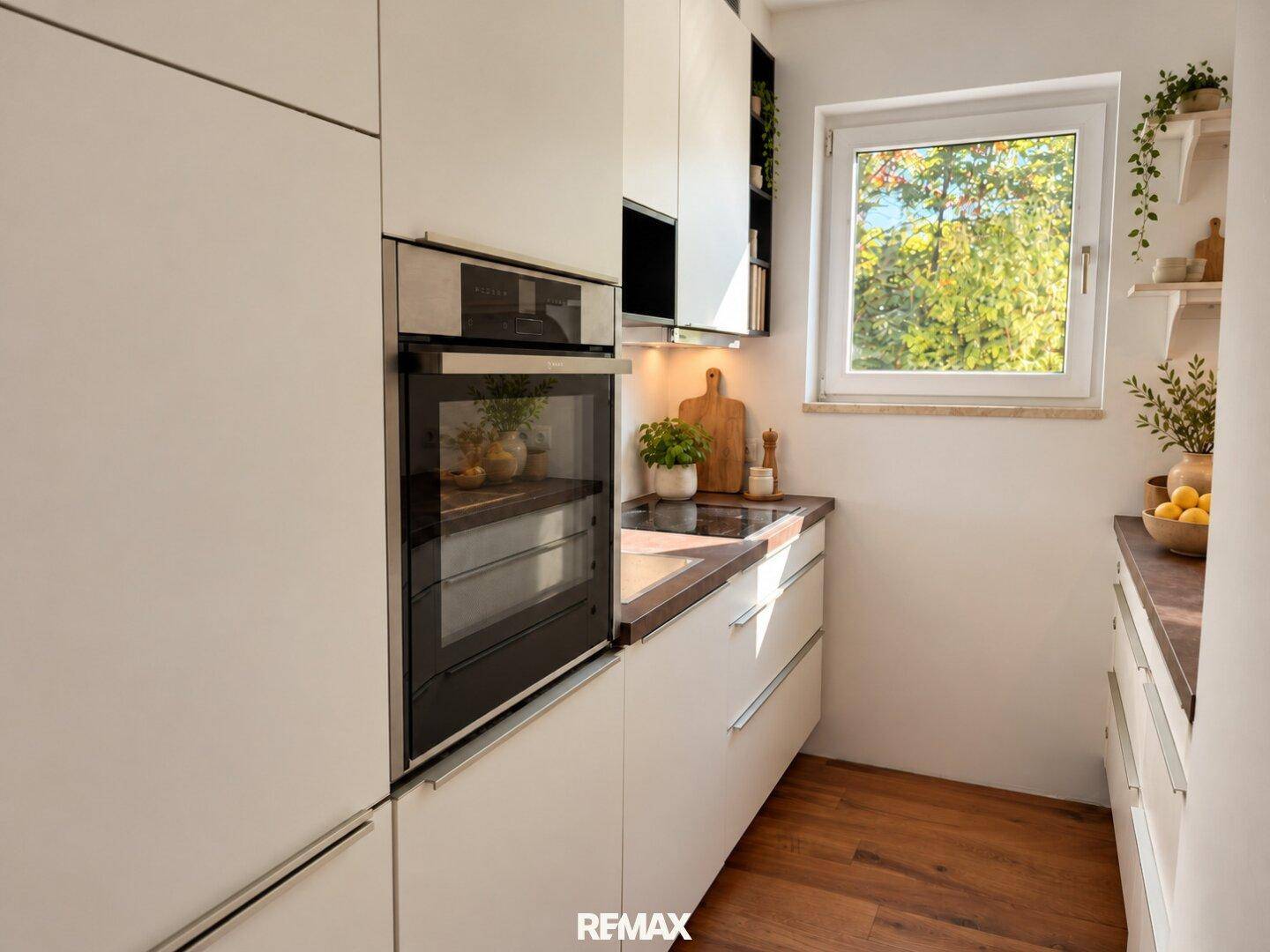 Moderne Einbauküche mit weißen Schränken, integriertem Backofen und Fenster mit Blick ins Grüne.