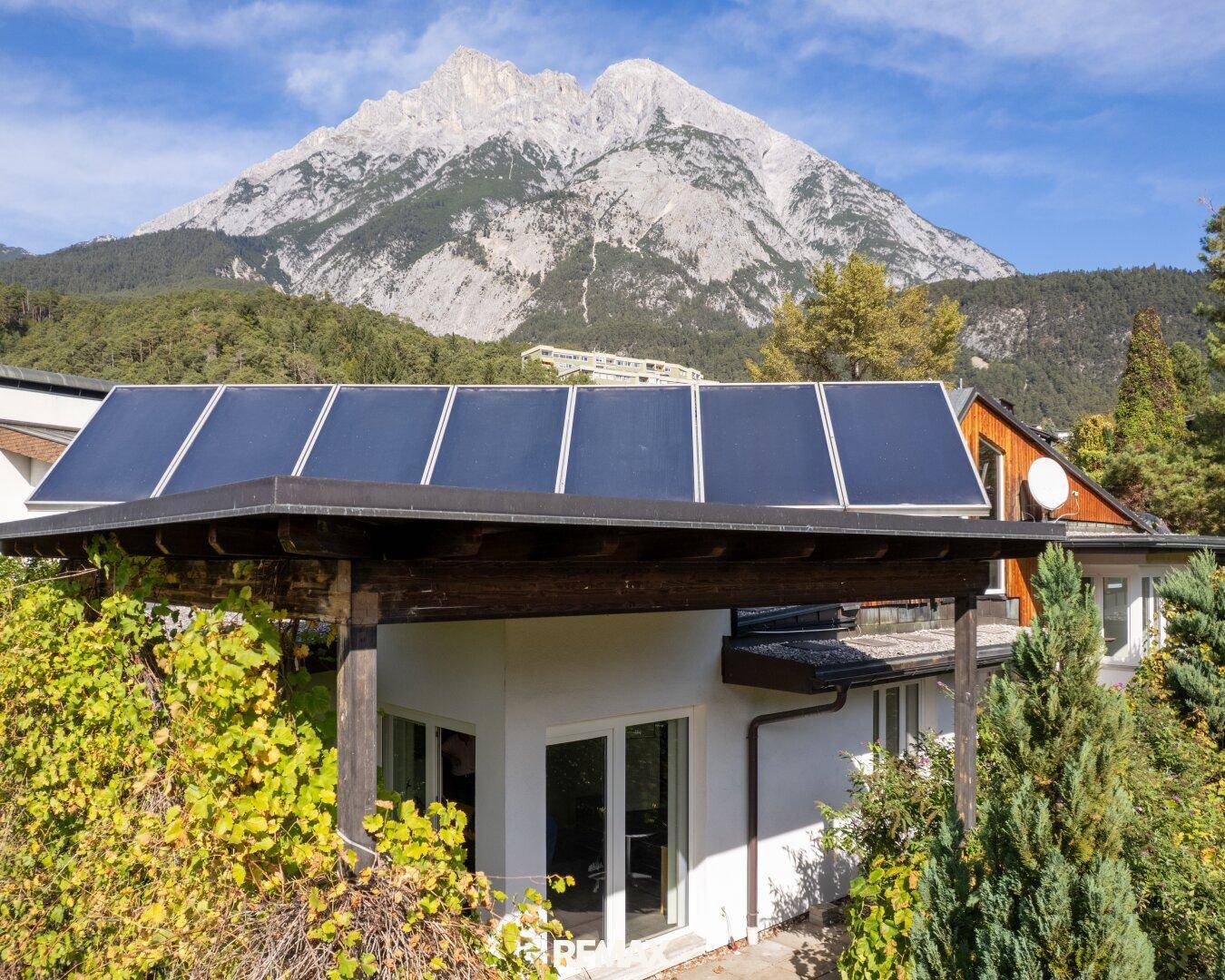 Nahaufnahme der Hausfassade mit Photovoltaikanlage und dem majestätischen Bergpanorama im Hintergrund.