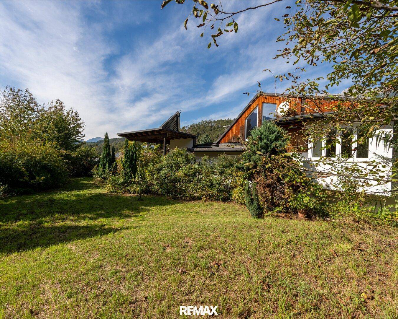 Weitläufiger Gartenbereich mit Rasenfläche und Blick auf das Haus vor der Bergkulisse.