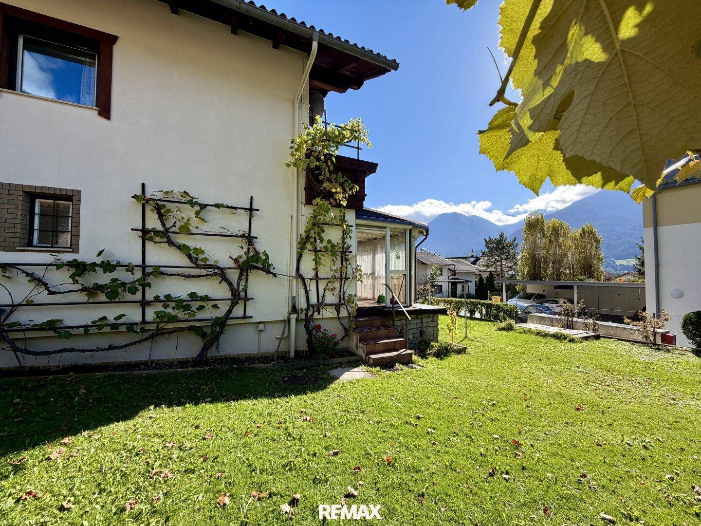 Sonnige Gartenseite des Hauses mit Kletterpflanzen an der Fassade und Bergblick.