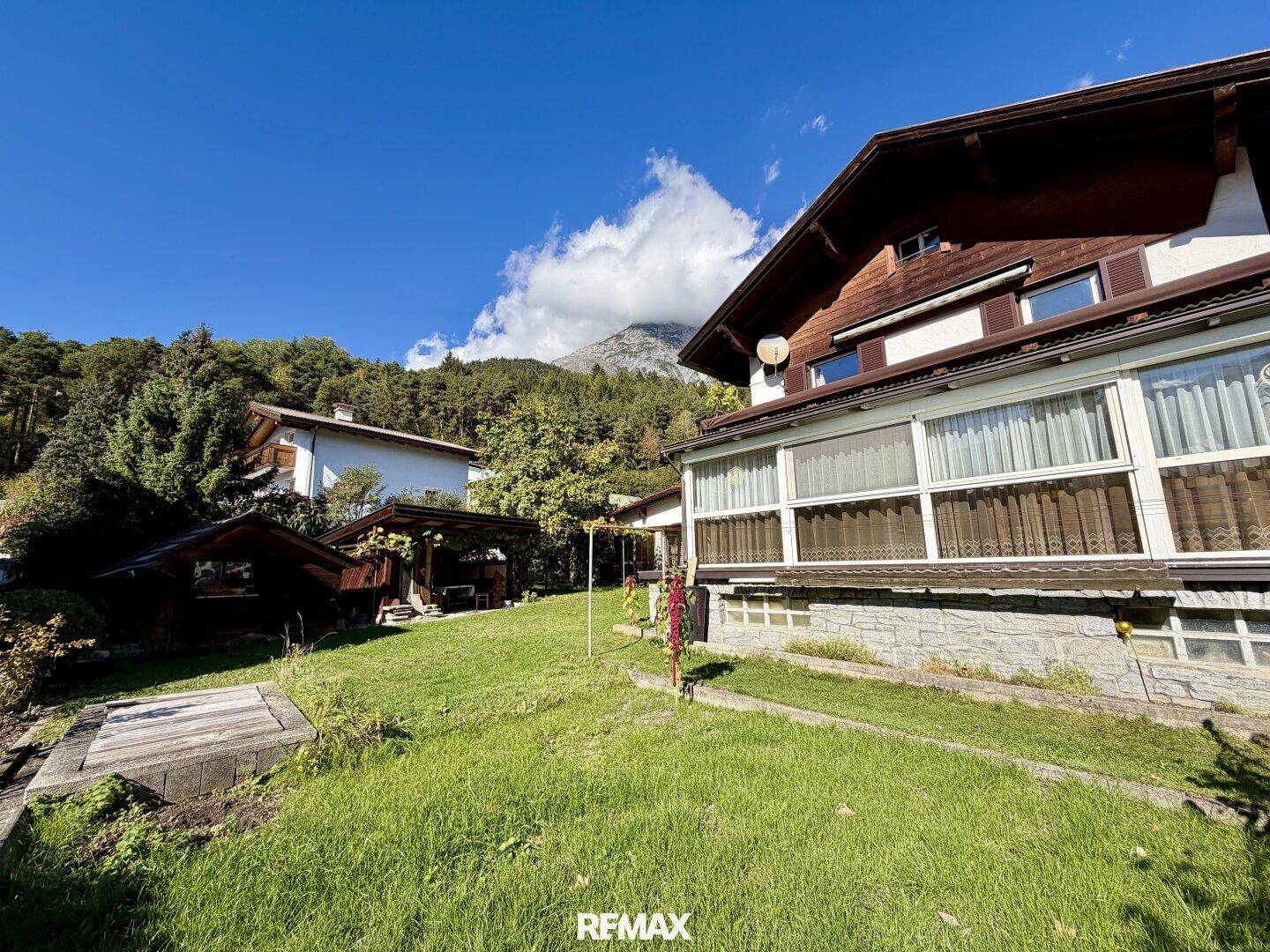 Seitenansicht des Hauses mit gepflegtem Rasen, Gartenbereich und Bergblick im Hintergrund.