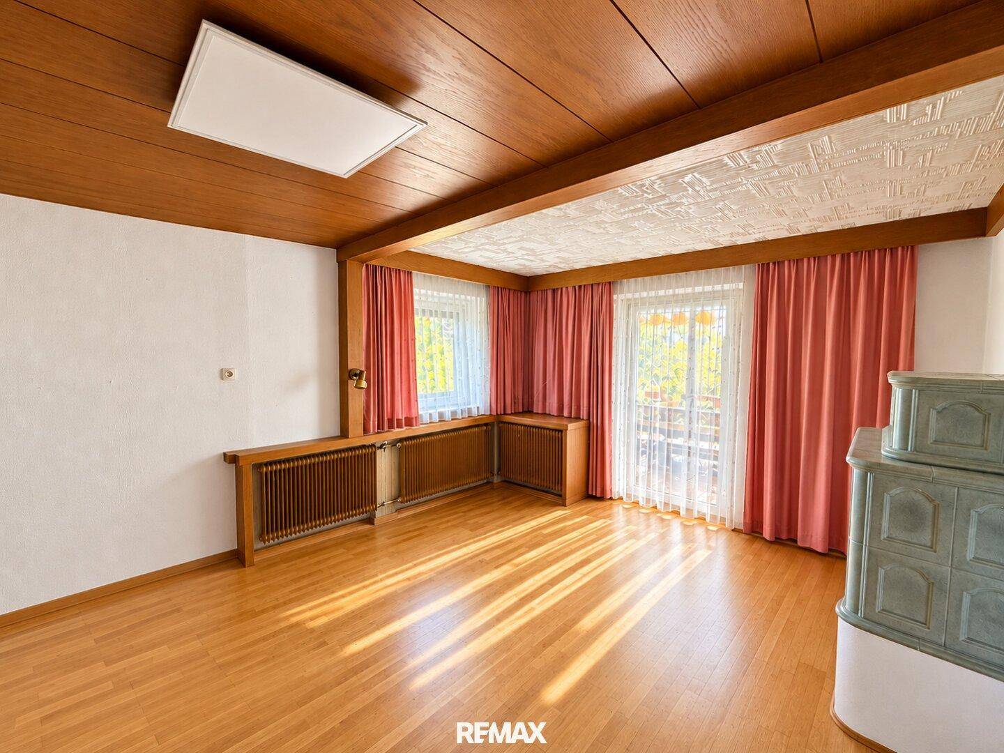 Gemütliches Wohnzimmer mit Holzbalkendecke, Parkettboden und traditionellem Kachelofen.