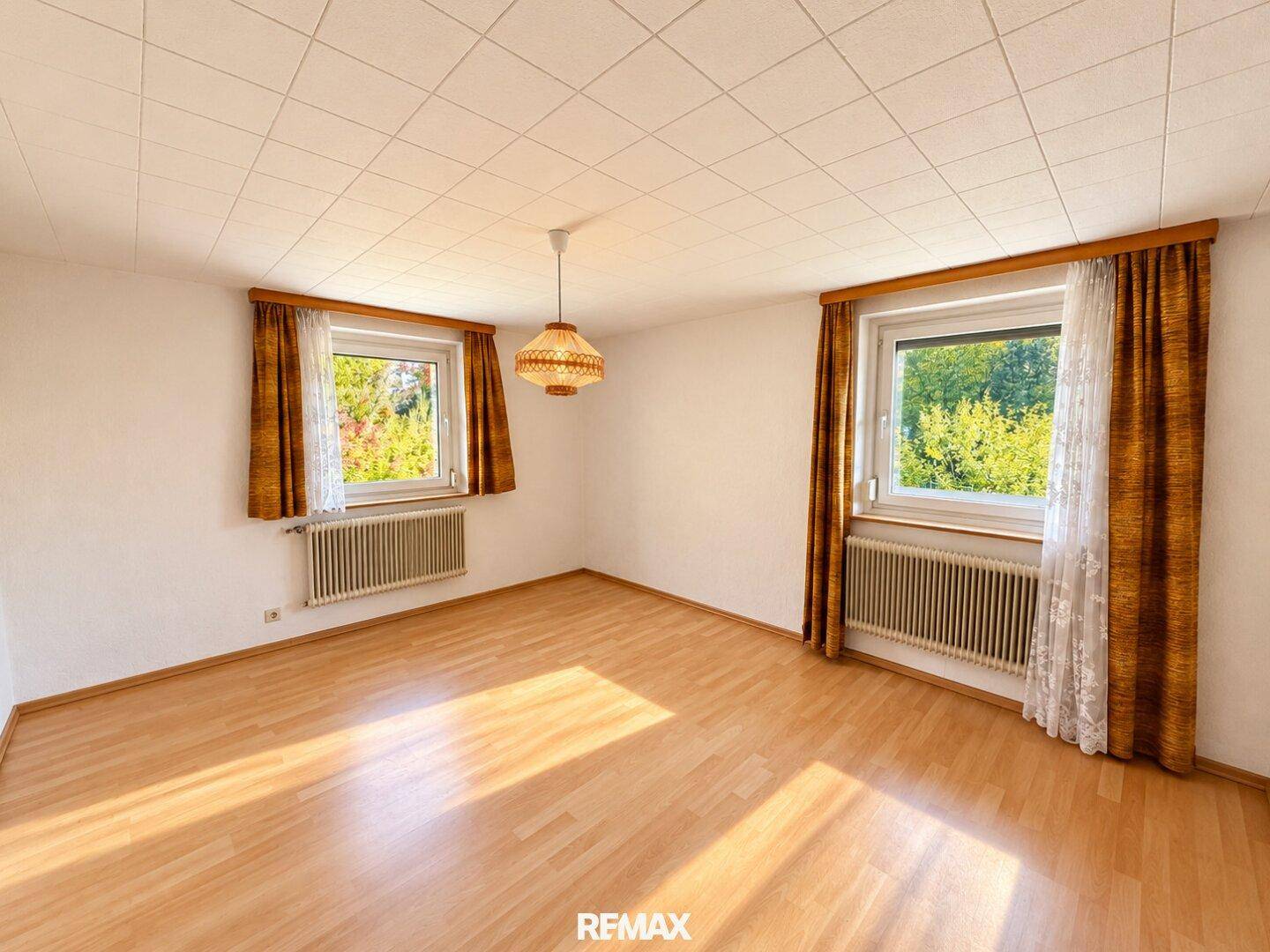 Geräumiges Schlafzimmer mit Parkettboden, zwei Fenstern und Blick ins Grüne.