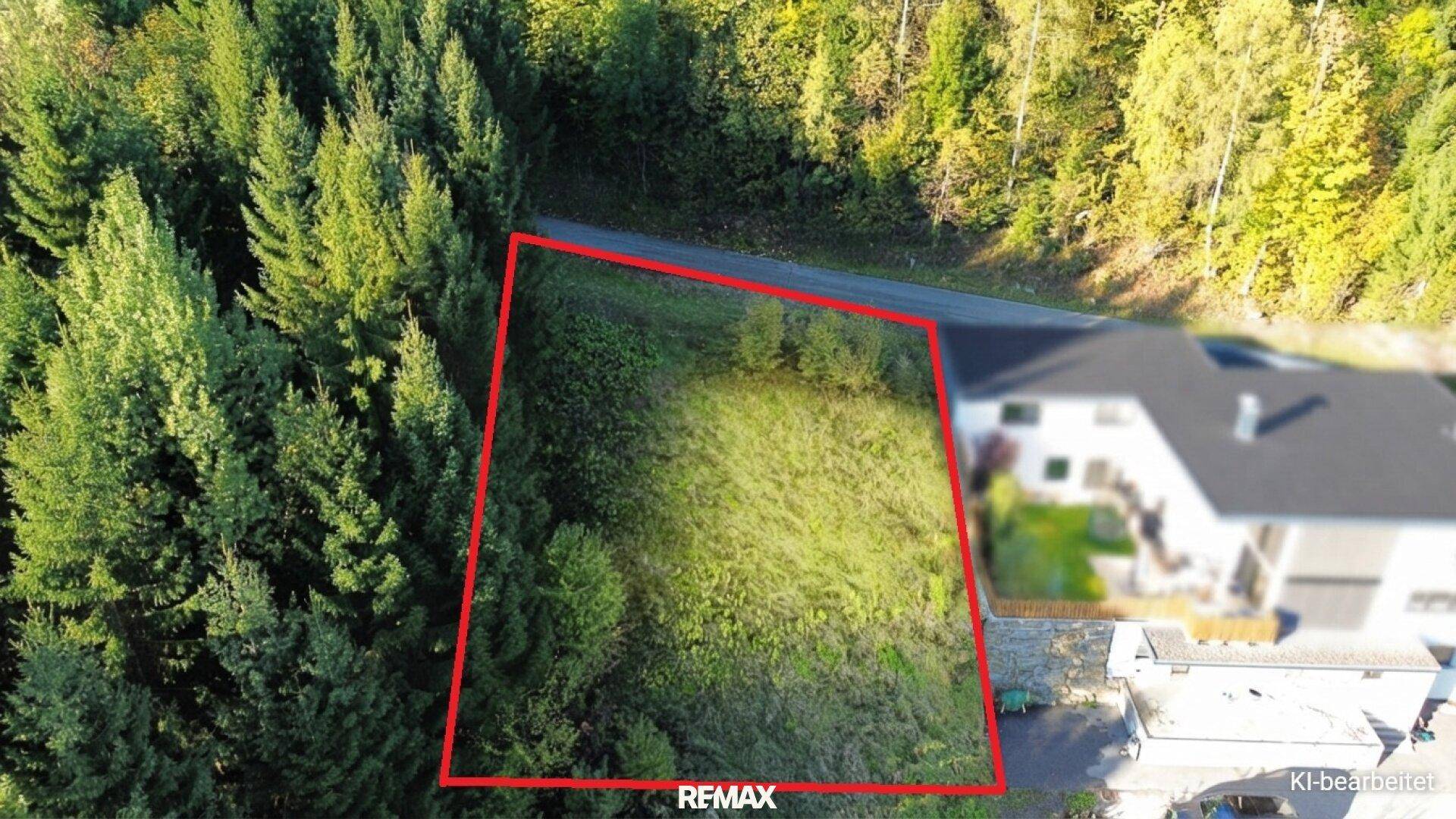 Luftaufnahme eines Baugrundstücks, rot umrandet, umgeben von Wald und einem Wohnhaus.