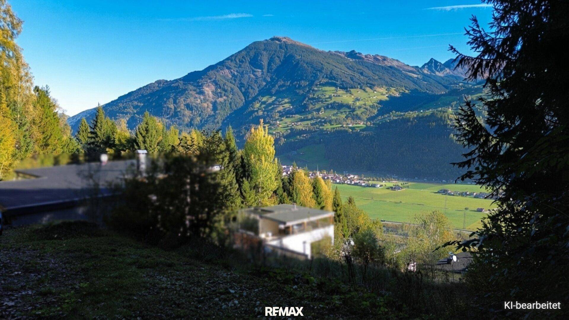 Weitläufiger Blick auf die Alpenlandschaft mit grünen Hügeln und einem Dorf im Tal.