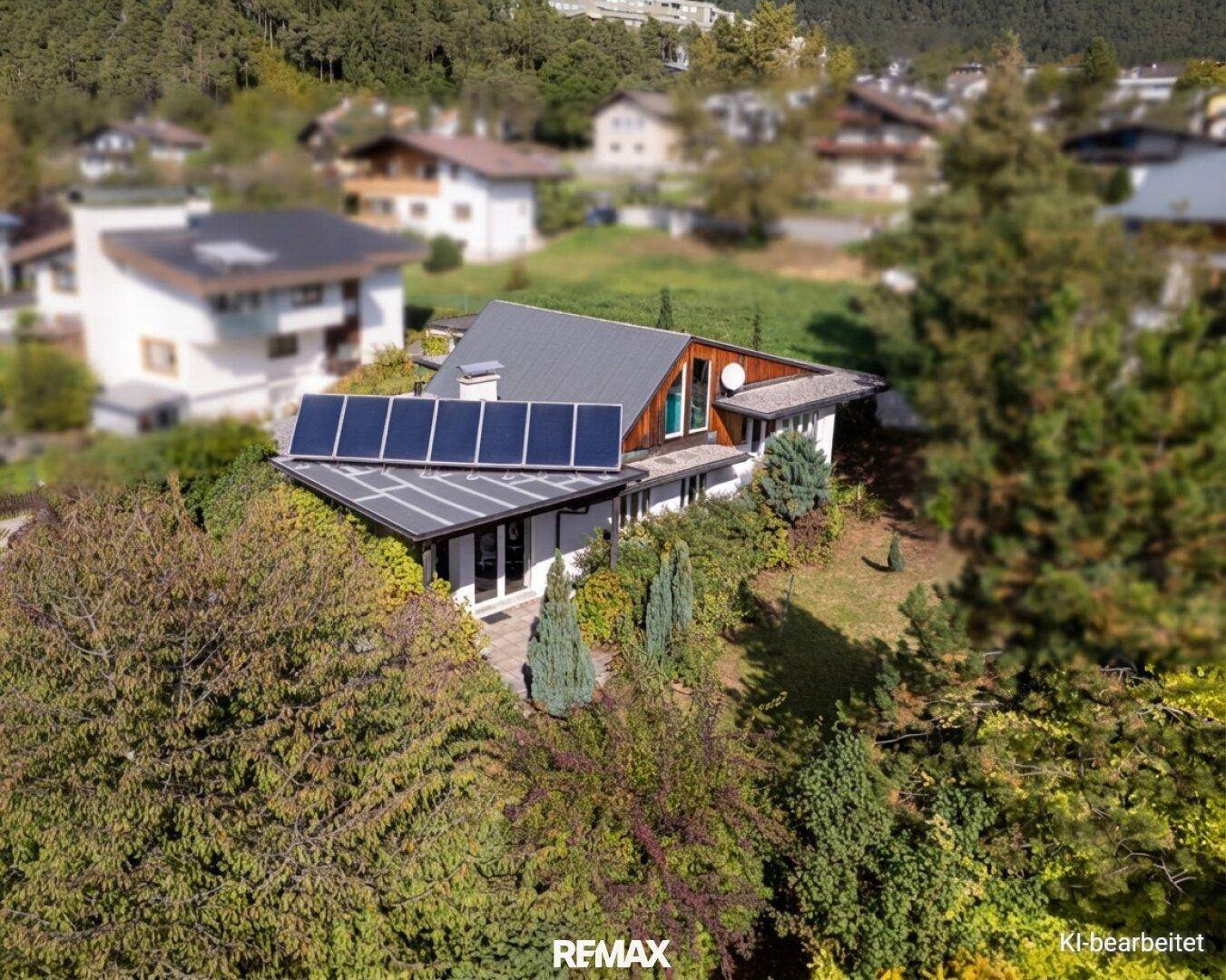 Luftaufnahme des Hauses mit Photovoltaikanlage auf dem Dach und umgebender grüner Landschaft.