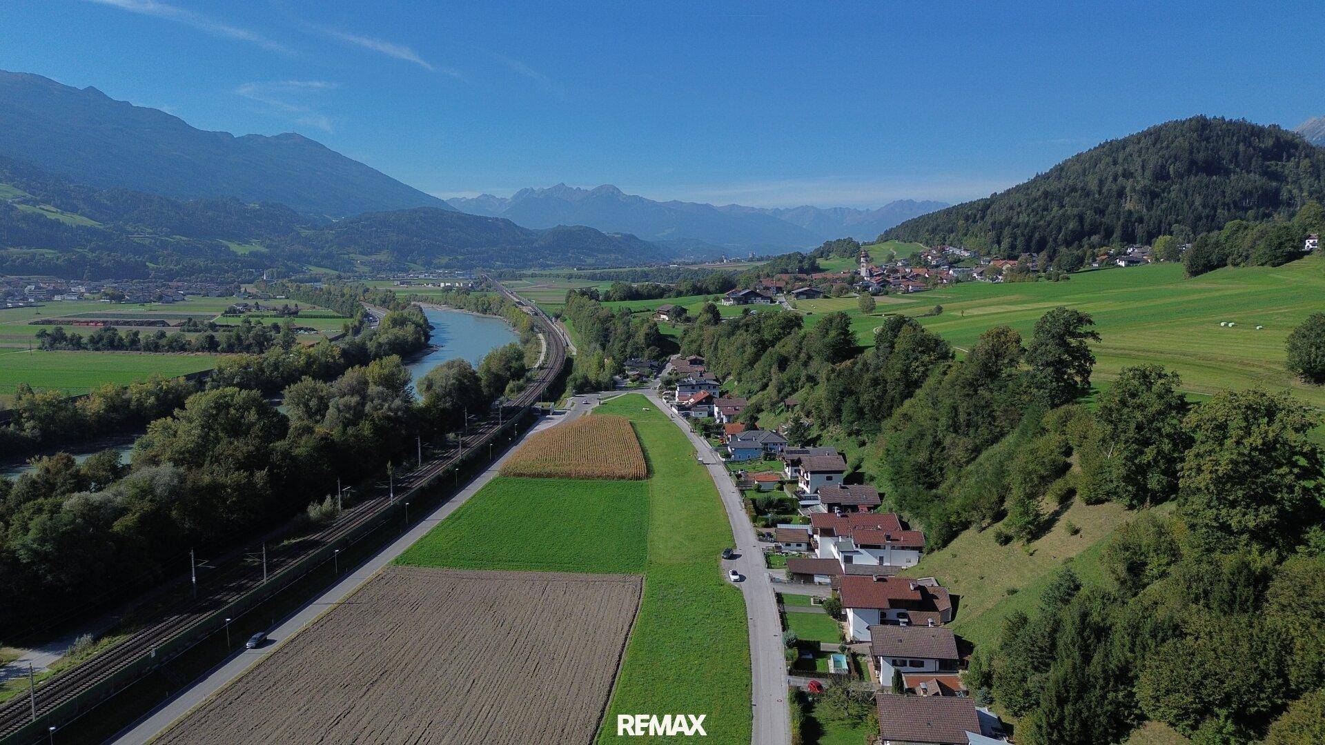 Panoramablick auf ein Flusstal mit Siedlung, umgeben von grünen Hügeln und Bergen.