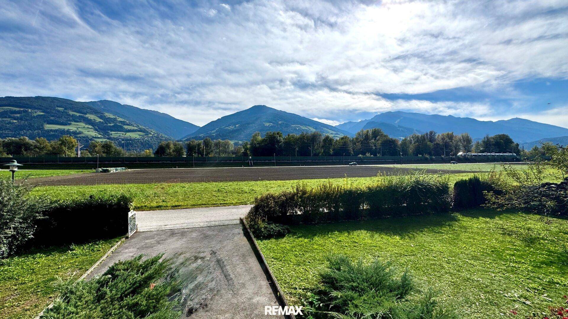 Weitblick auf grüne Felder und majestätische Berge unter einem bewölkten Himmel.
