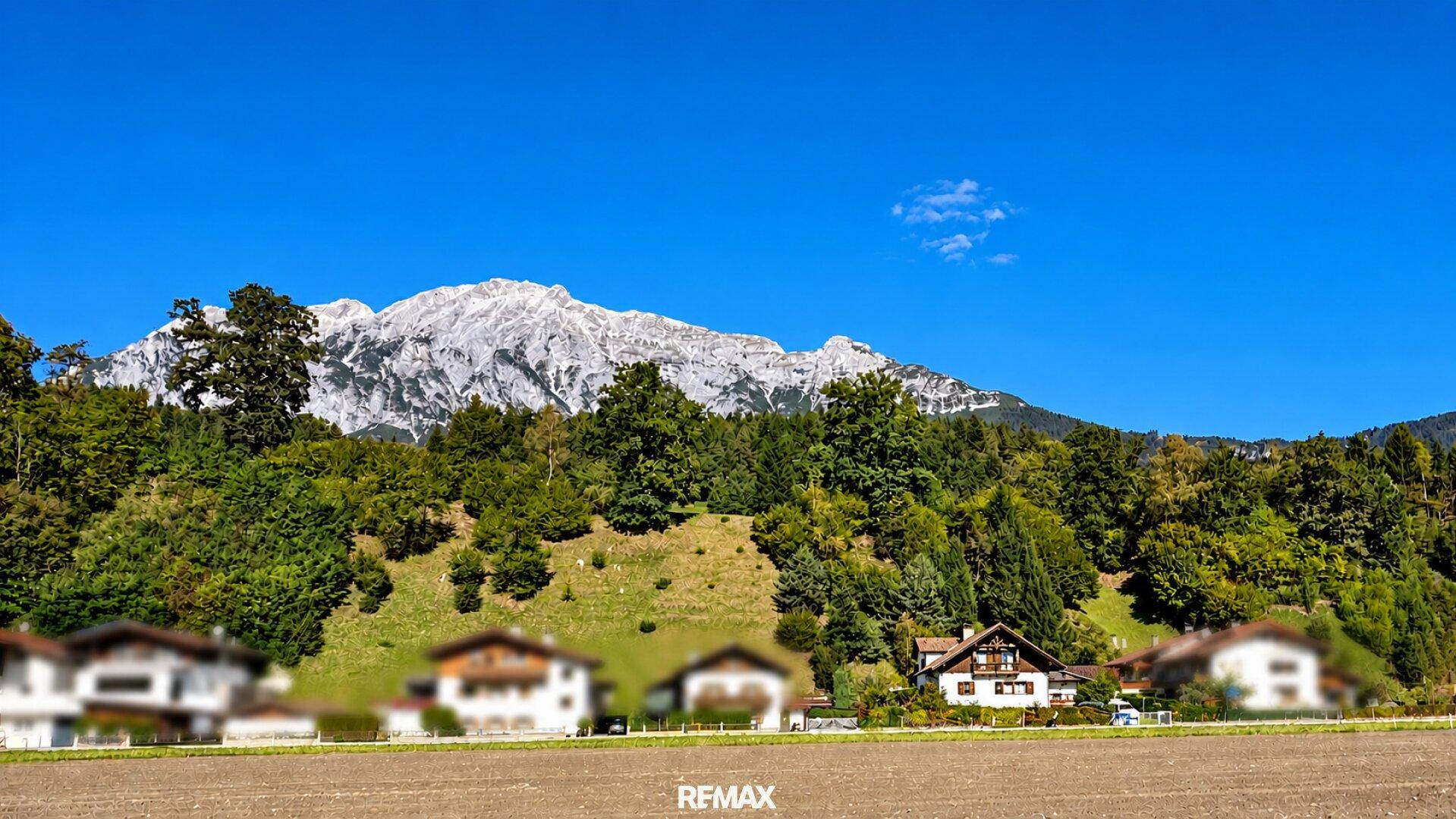 Malerische Berglandschaft mit schneebedeckten Gipfeln und grünen Wäldern unter blauem Himmel.