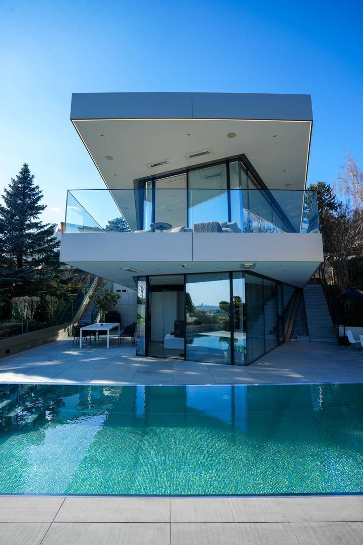 Architektonisch anspruchsvolle Villa mit Infinity-Pool und großen Glasfronten unter blauem Himmel.