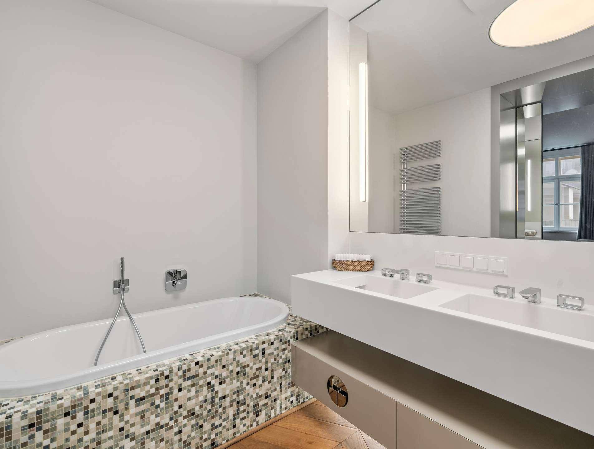 Modernes Badezimmer mit Doppelwaschbecken, Badewanne und Mosaikfliesen an der Wannenverkleidung.
