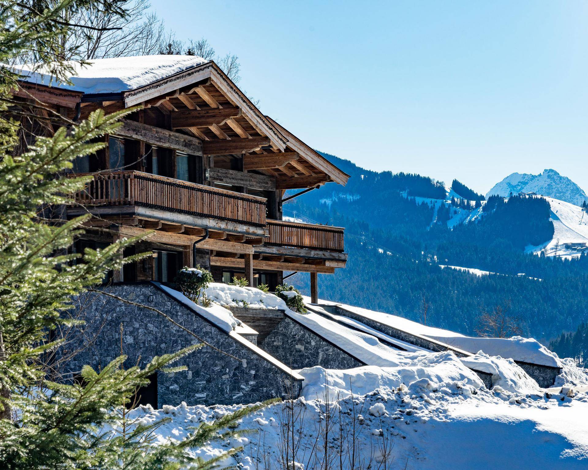 Traditionelles Chalet mit Holzbalkonen und Steinfundament in verschneiter Berglandschaft.