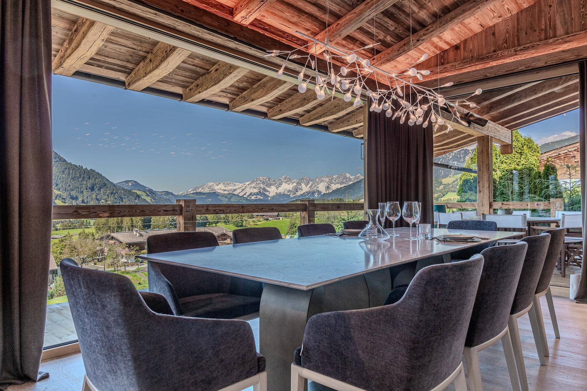 Eleganter Essbereich mit großem Tisch, moderner Beleuchtung und Panoramablick auf die Berge.