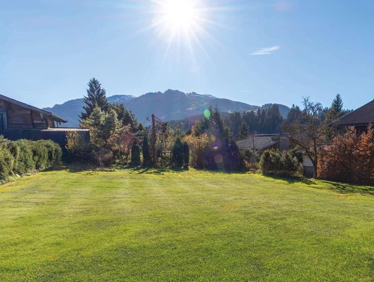 Sonniger Gartenbereich mit weitläufiger Rasenfläche und Blick auf die umliegenden Berge.