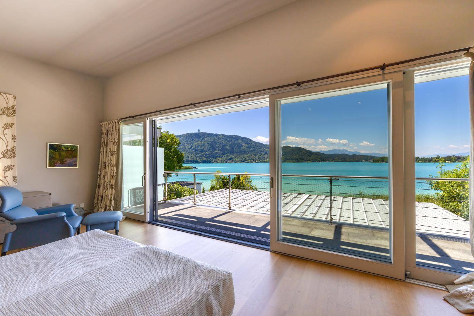 Schlafzimmer mit Holzboden, großen Fenstern und atemberaubendem Blick auf den See und die umliegende Landschaft.