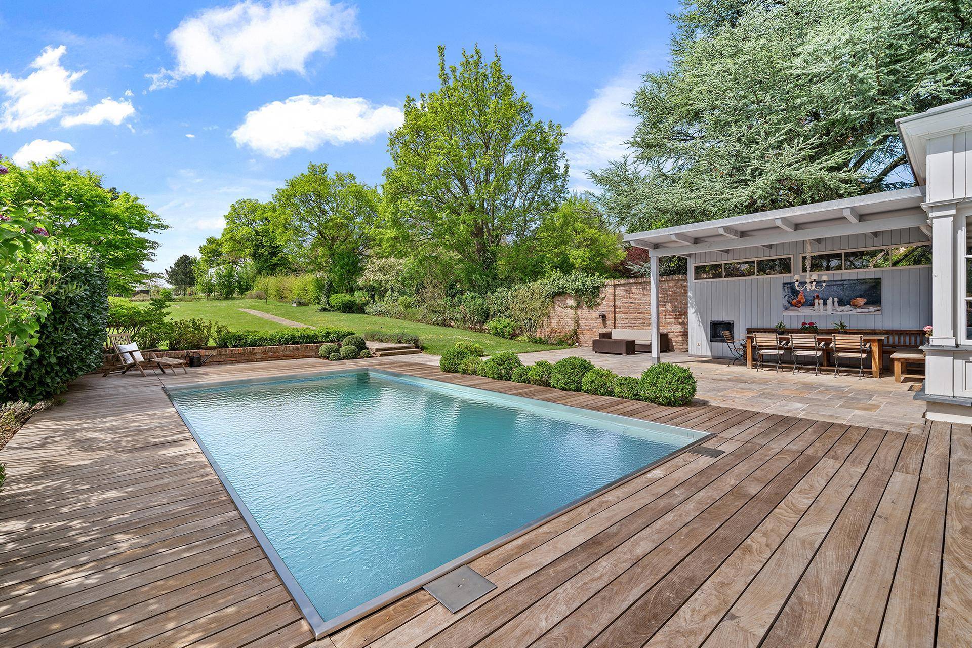 Großzügiger Gartenbereich mit Swimmingpool, Holzterrasse und gemütlichem Essplatz unter einer Pergola.