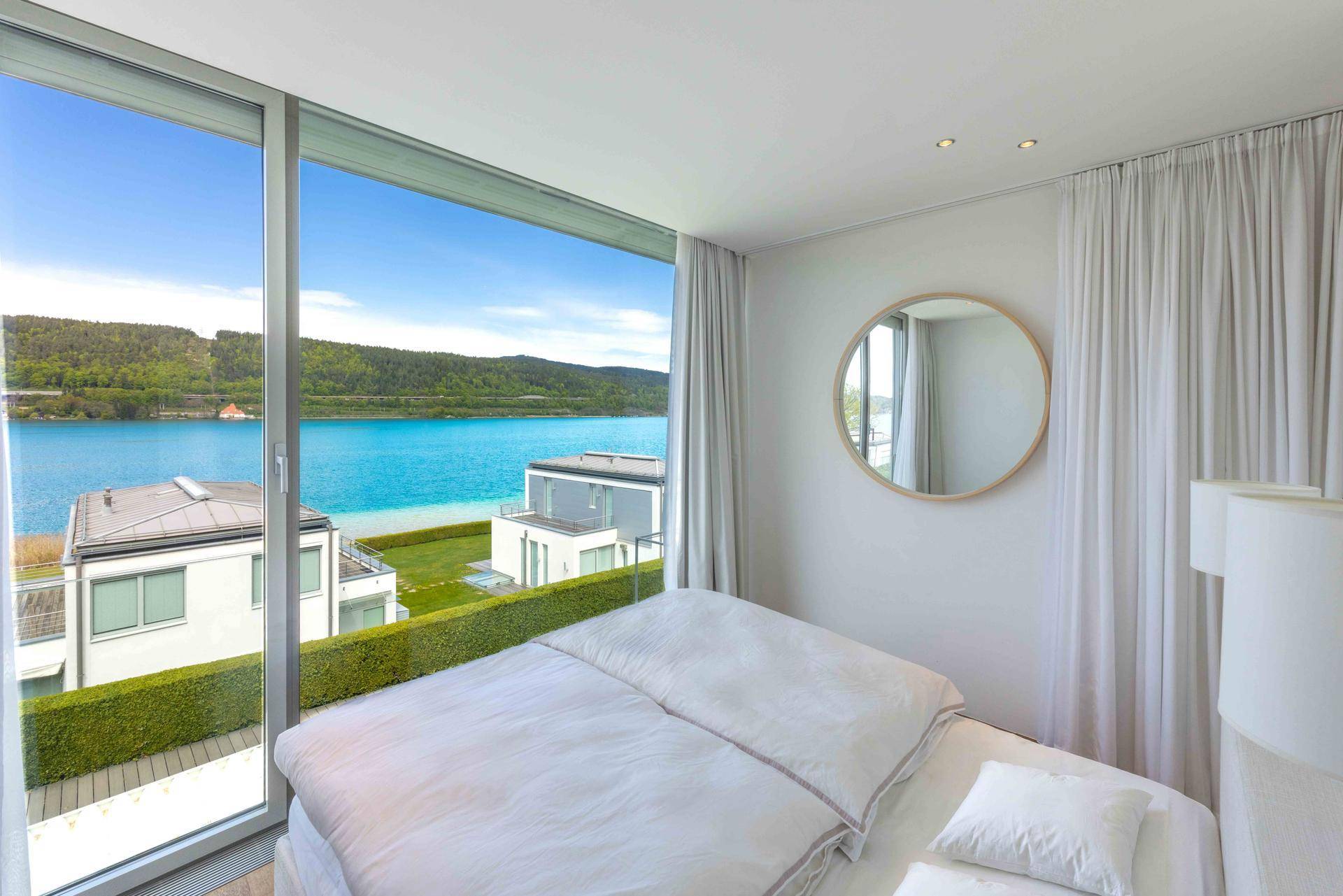 Schlafzimmer mit atemberaubendem Seeblick durch raumhohe Fenster und minimalistischer Einrichtung.
