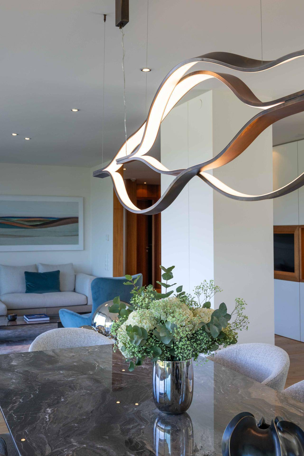 Eleganter Essbereich mit modernem Design-Kronleuchter und Blick in den Wohnbereich.