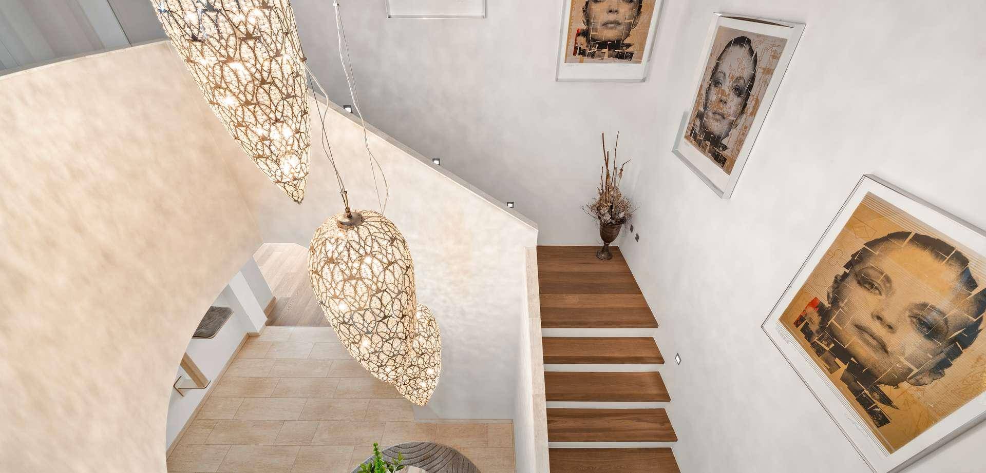 Elegantes Treppenhaus mit Holzstufen, modernen Leuchten und Kunstwerken an der Wand.