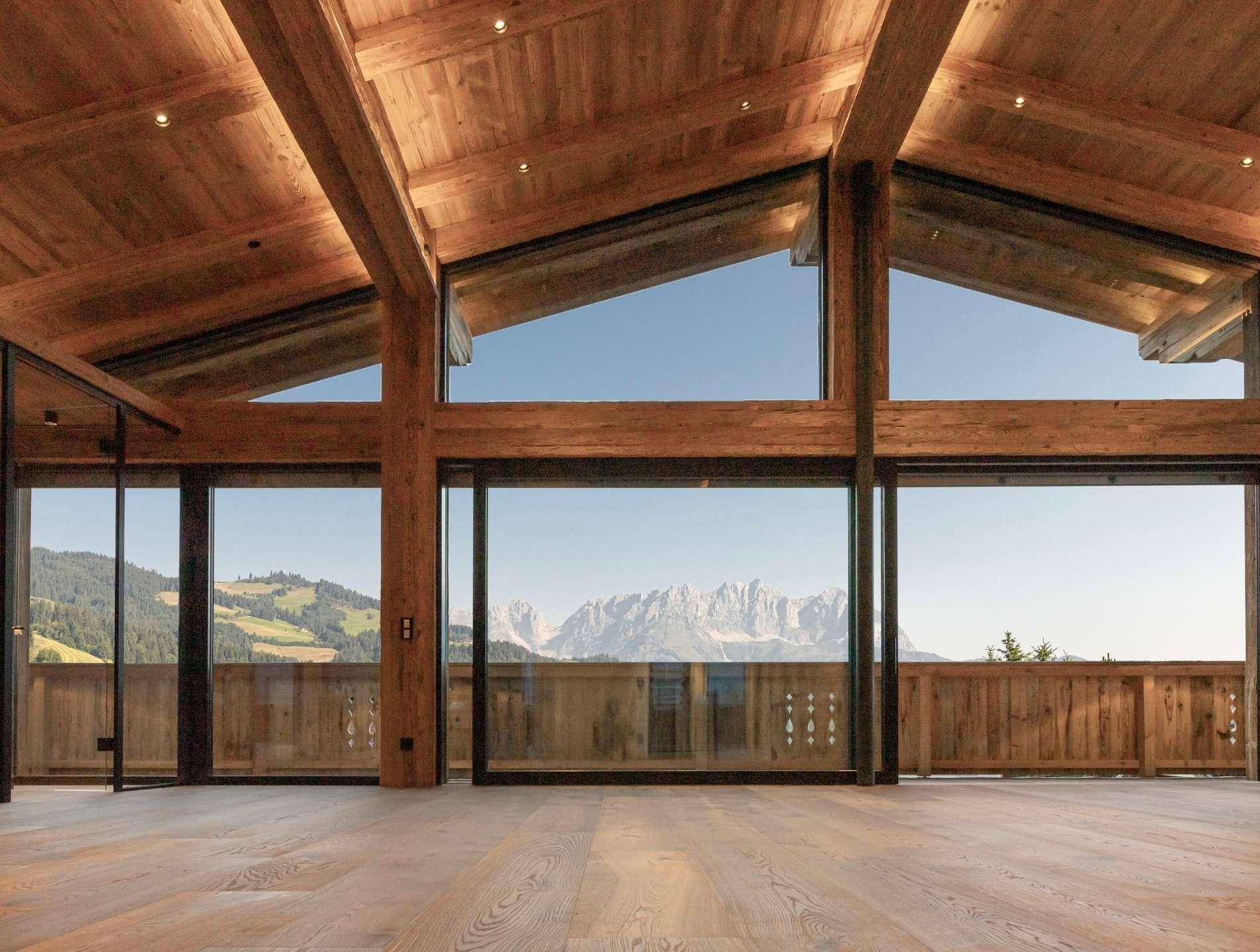 Heller Wohnbereich mit Holzbalkendecke und raumhohen Fenstern, die einen weiten Bergblick bieten.