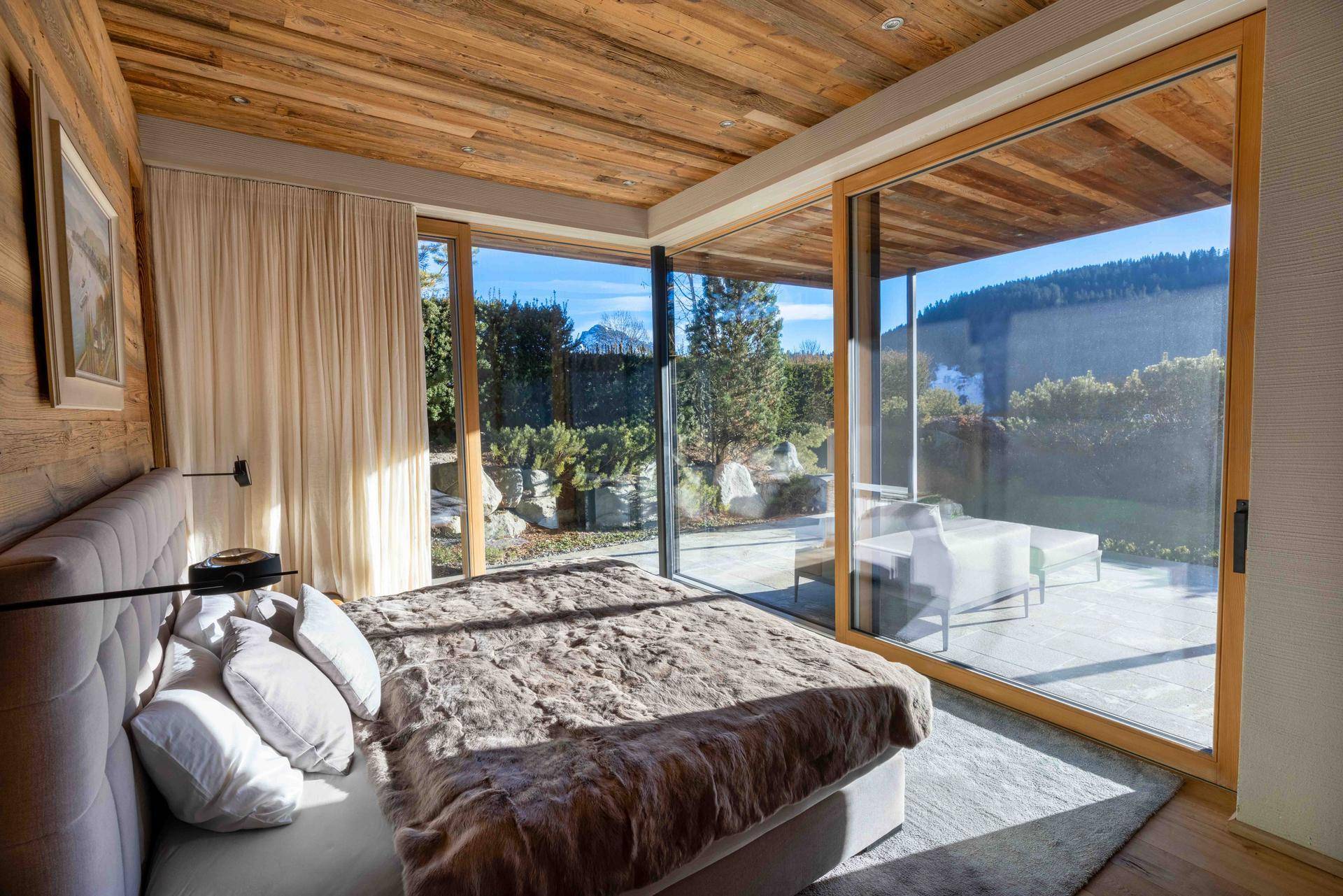 Gemütliches Schlafzimmer mit großen Schiebetüren zum Garten und Holzbalkendecke.