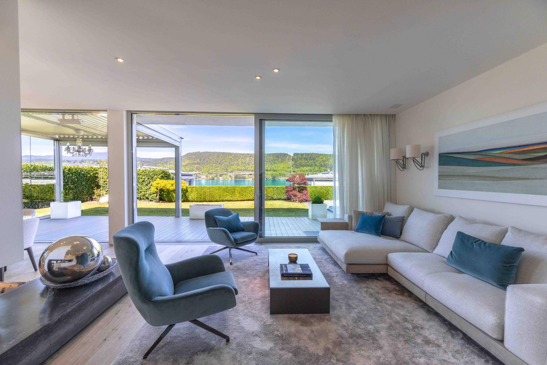 Helles Wohnzimmer mit bequemen Sofas, Teppich und direktem Zugang zur Terrasse mit Seeblick.