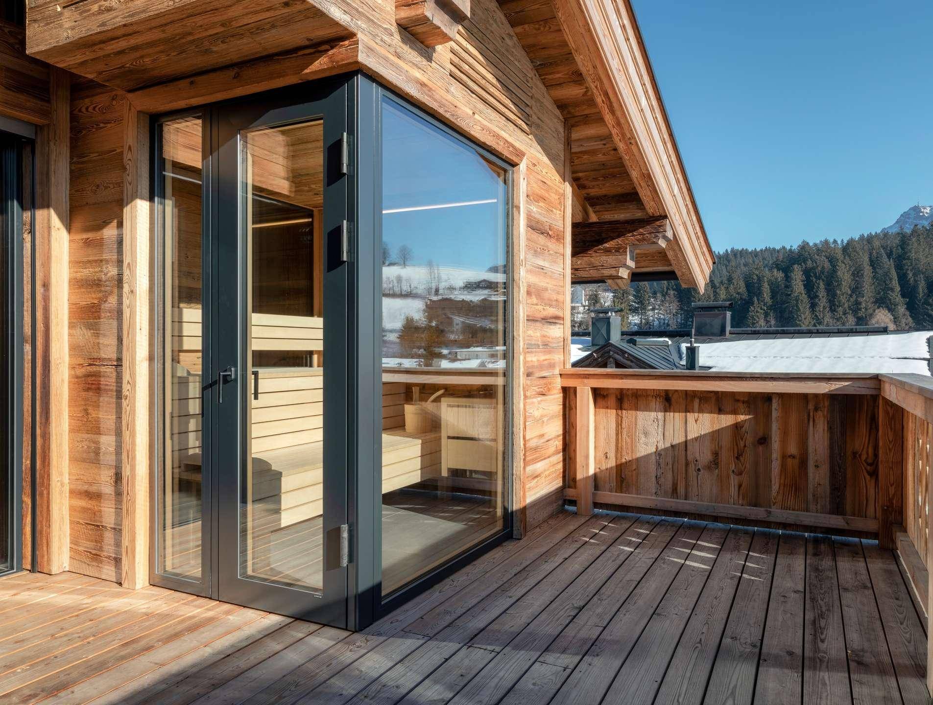Holzbalkon mit Blick auf die verschneite Landschaft und Zugang zu einer sichtbaren Sauna.