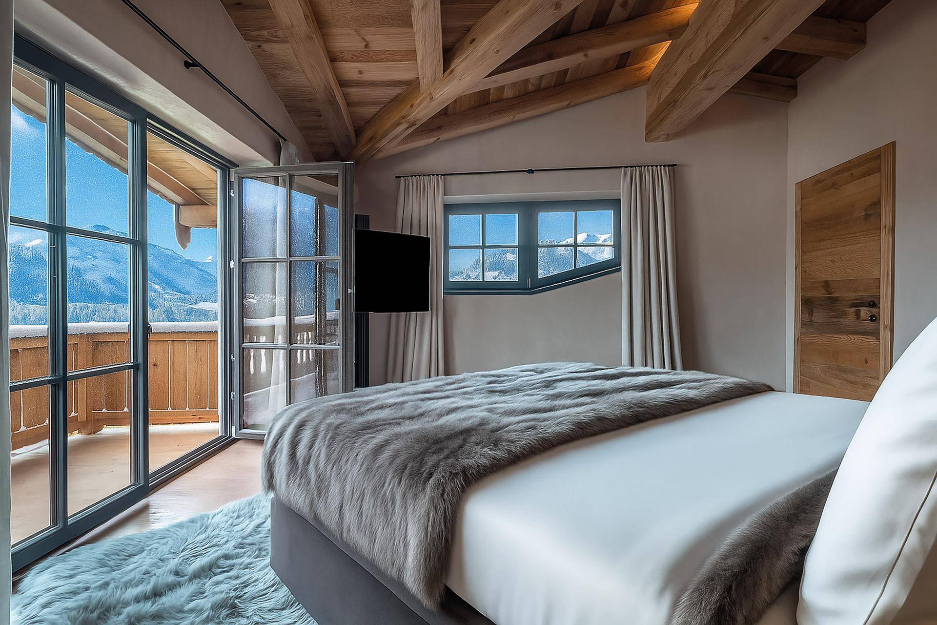 Gemütliches Schlafzimmer mit Holzbalkendecke, direktem Zugang zum Balkon und atemberaubendem Bergblick.