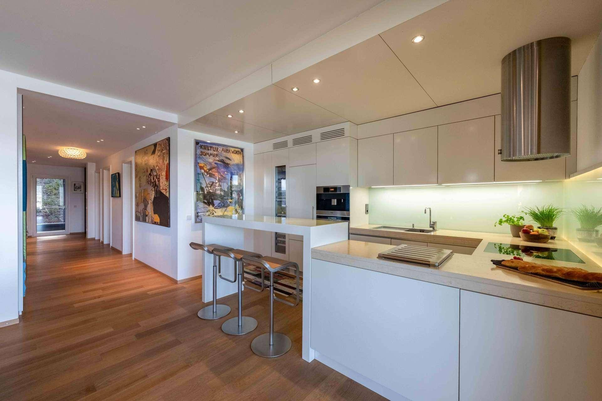 Moderne weiße Küche mit Kochinsel, Frühstücksbar und hellem Holzfußboden in offenem Grundriss.