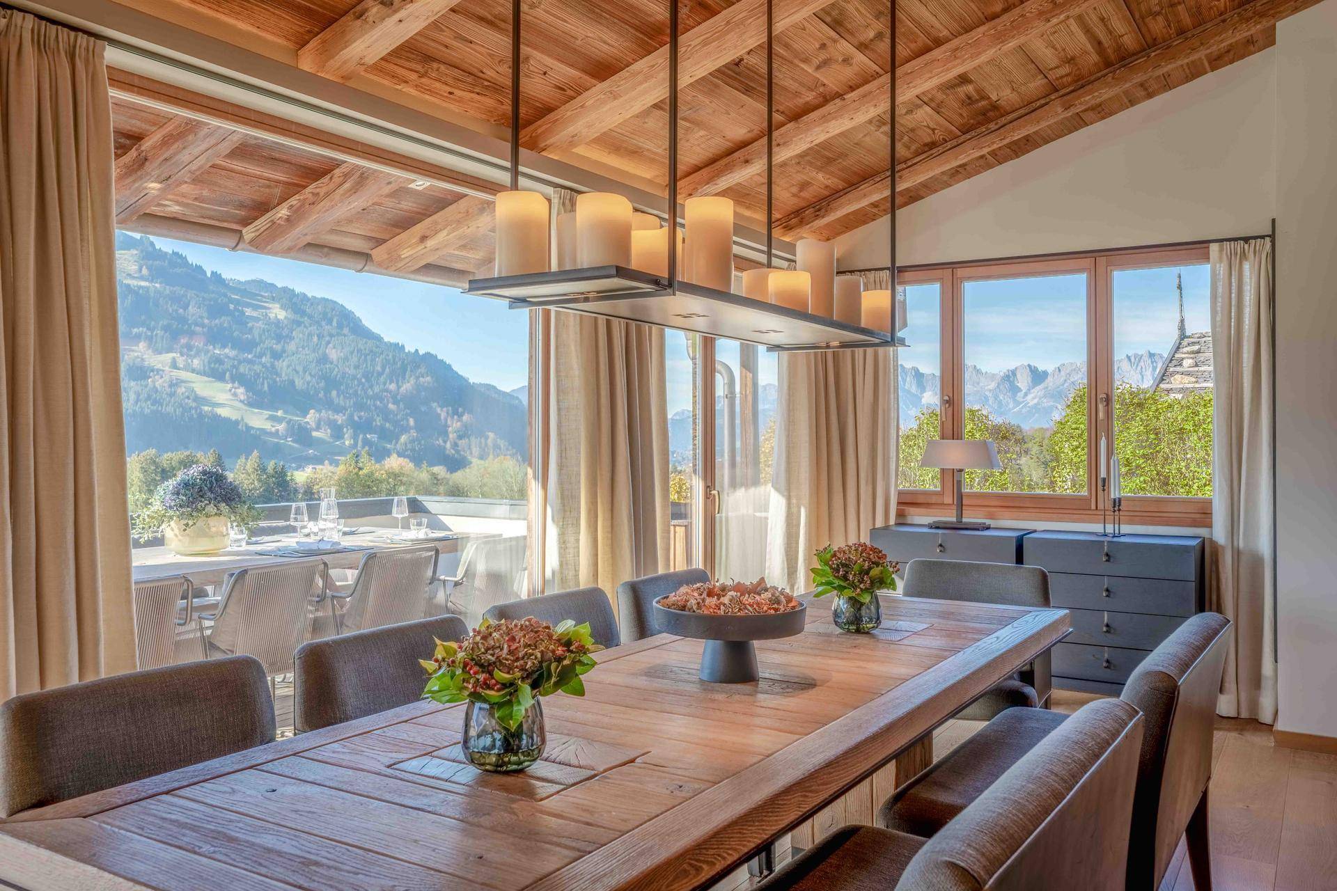 Eleganter Essbereich mit Holztisch, hohen Decken und Panoramafenstern mit Bergblick.