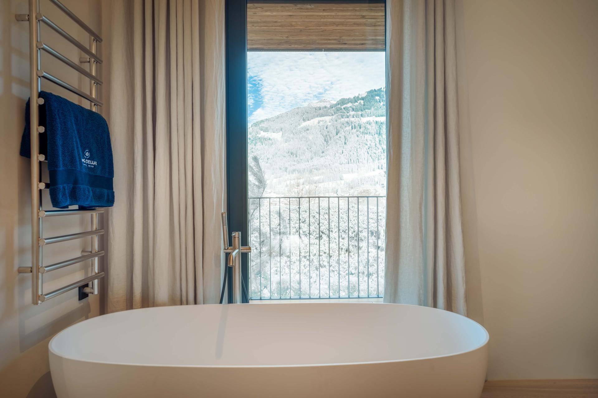 Modernes Badezimmer mit freistehender Badewanne, beheiztem Handtuchhalter und Bergblick durch das Fenster.
