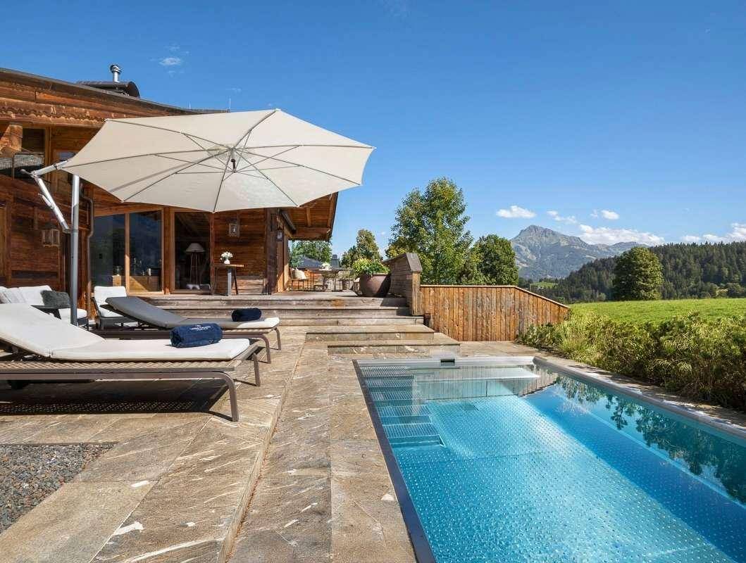 Sonniger Poolbereich mit Liegestühlen und weitem Blick über die grüne Landschaft und Berge.