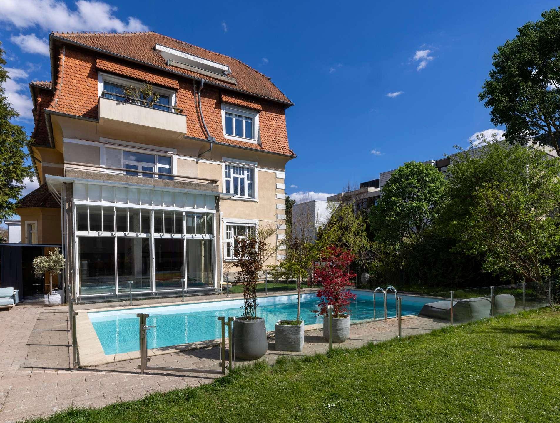 Hinterhof mit großem Swimmingpool, gepflegtem Rasen und sonniger Terrasse.
