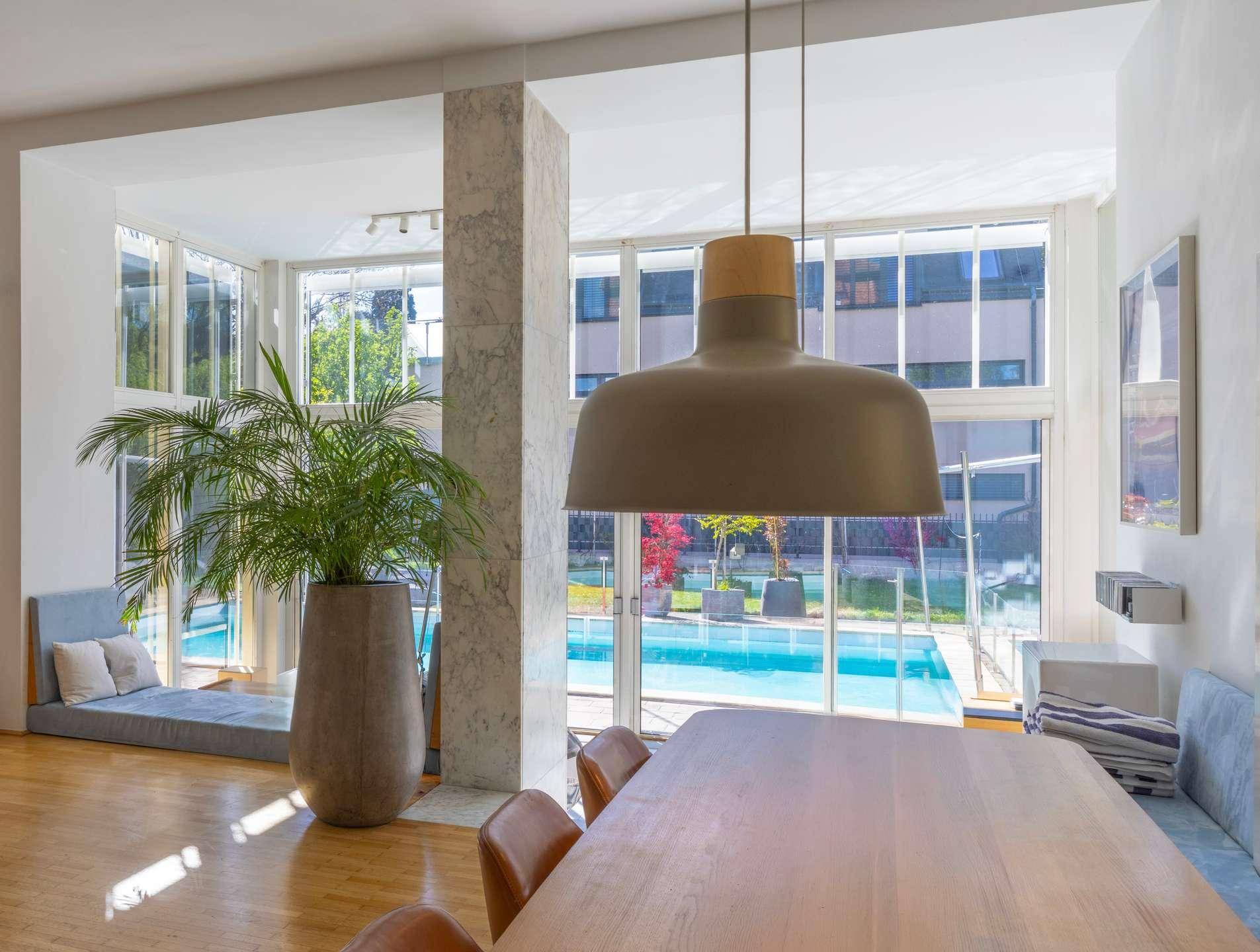 Heller Wohnbereich mit großen Fenstern, Blick auf den Pool und moderne Einrichtung.
