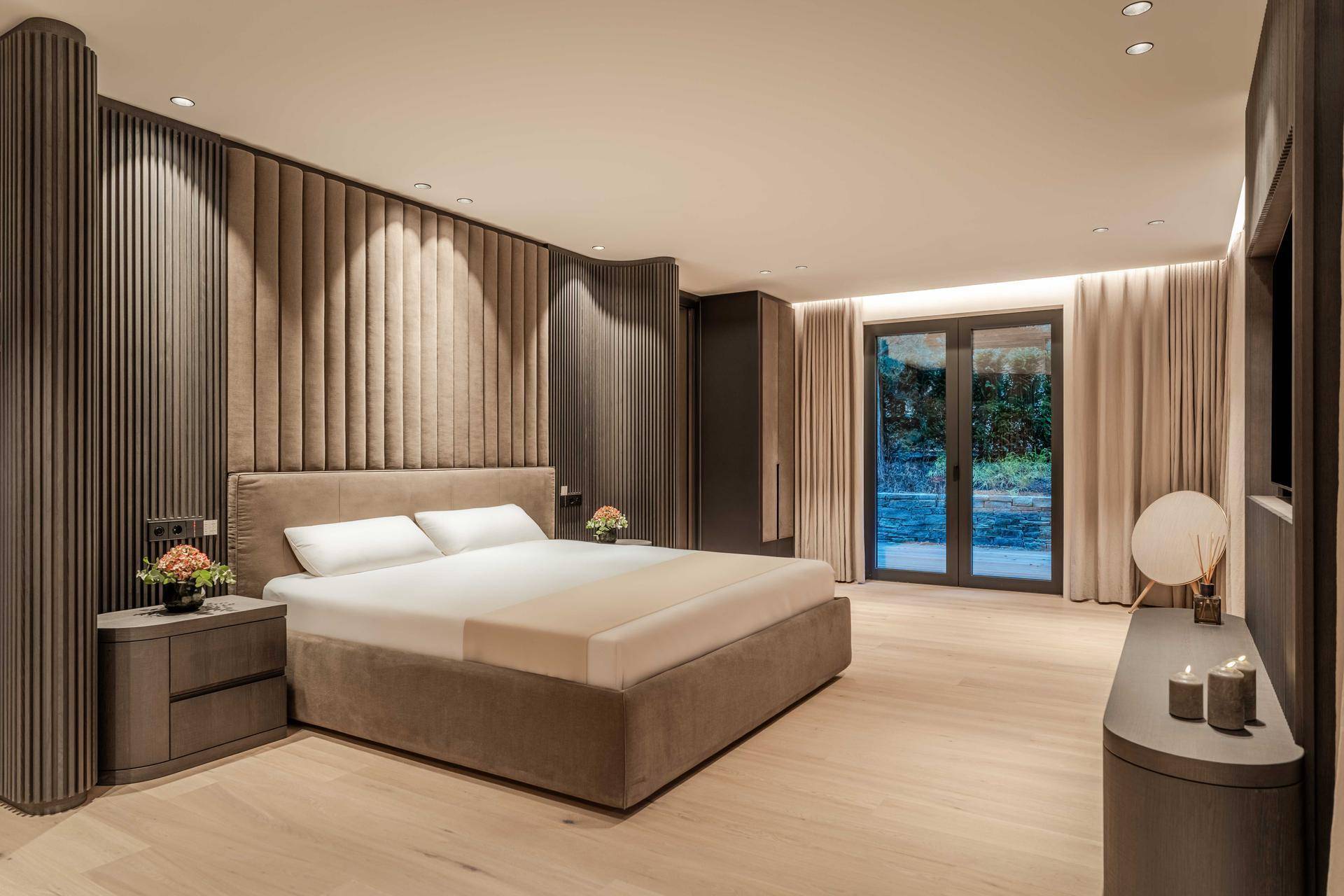Modernes Schlafzimmer mit gepolstertem Kopfteil, Holzboden und indirekter Beleuchtung.