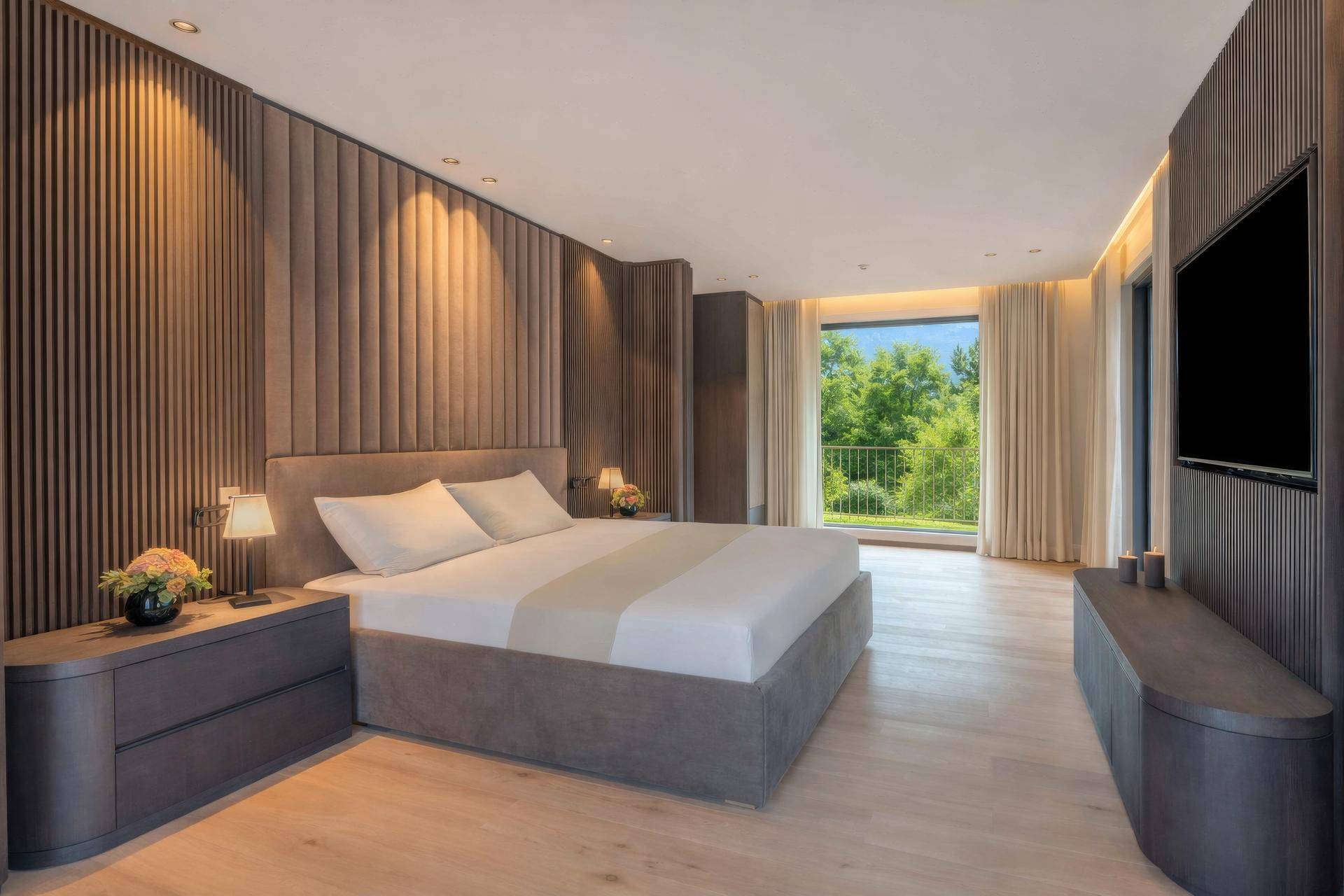 Modernes Schlafzimmer mit Holzboden, gepolsterter Wand und Zugang zu einem Balkon mit Grünblick.
