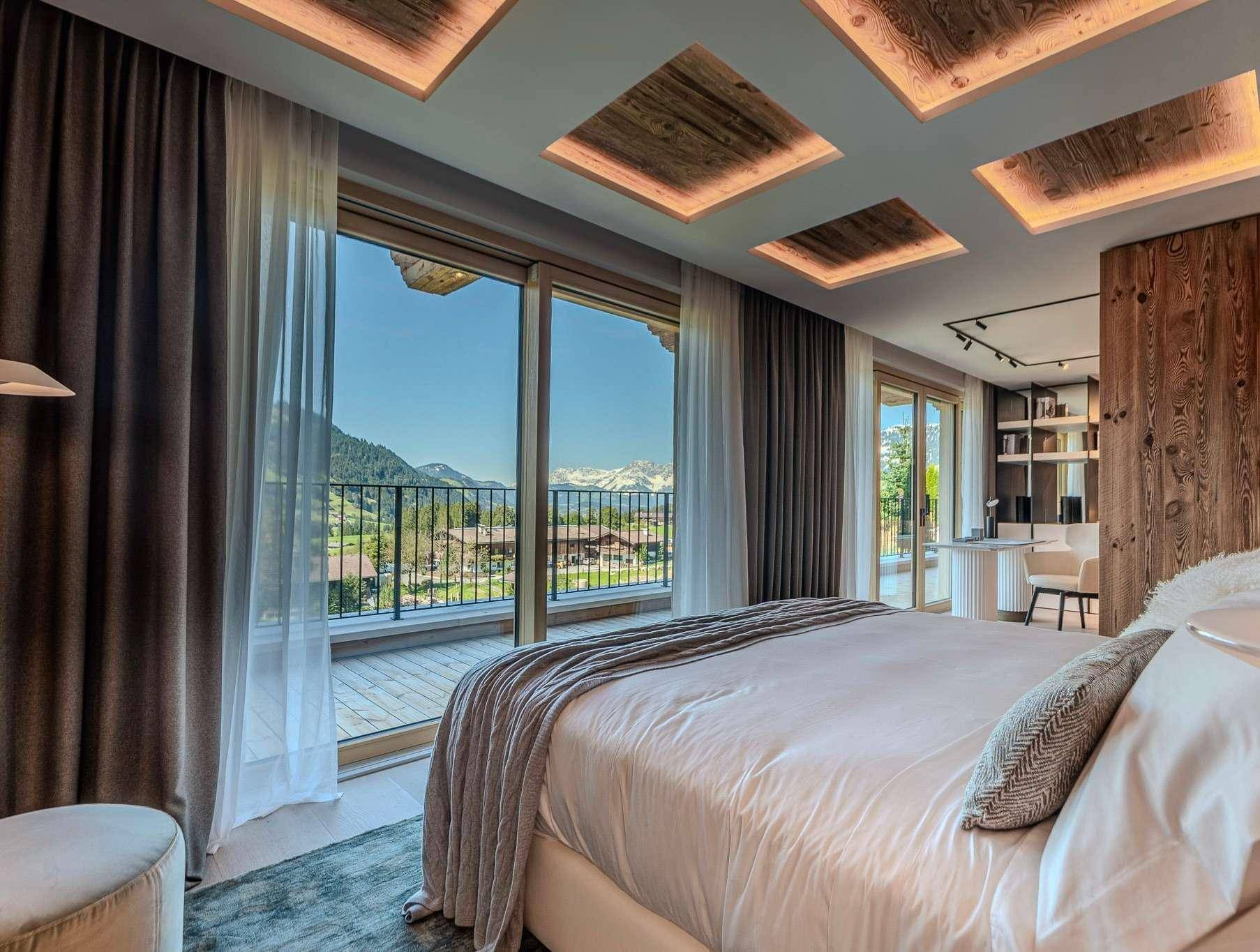 Helles Schlafzimmer mit großem Bett, Holzakzenten und Zugang zu einem Balkon mit Bergblick.