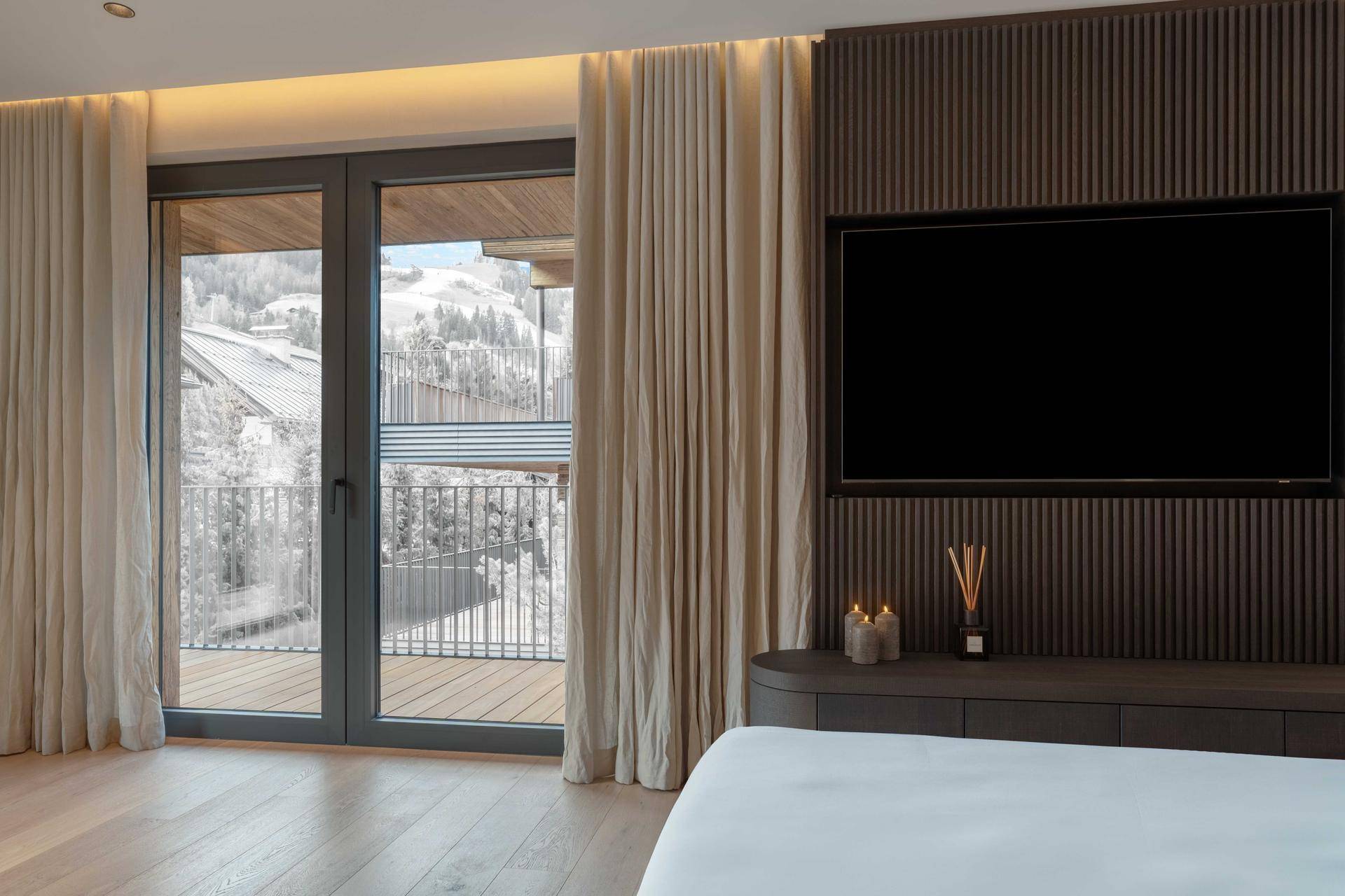 Schlafzimmer mit Balkonzugang, großem Fernseher und malerischem Blick auf die verschneite Berglandschaft.