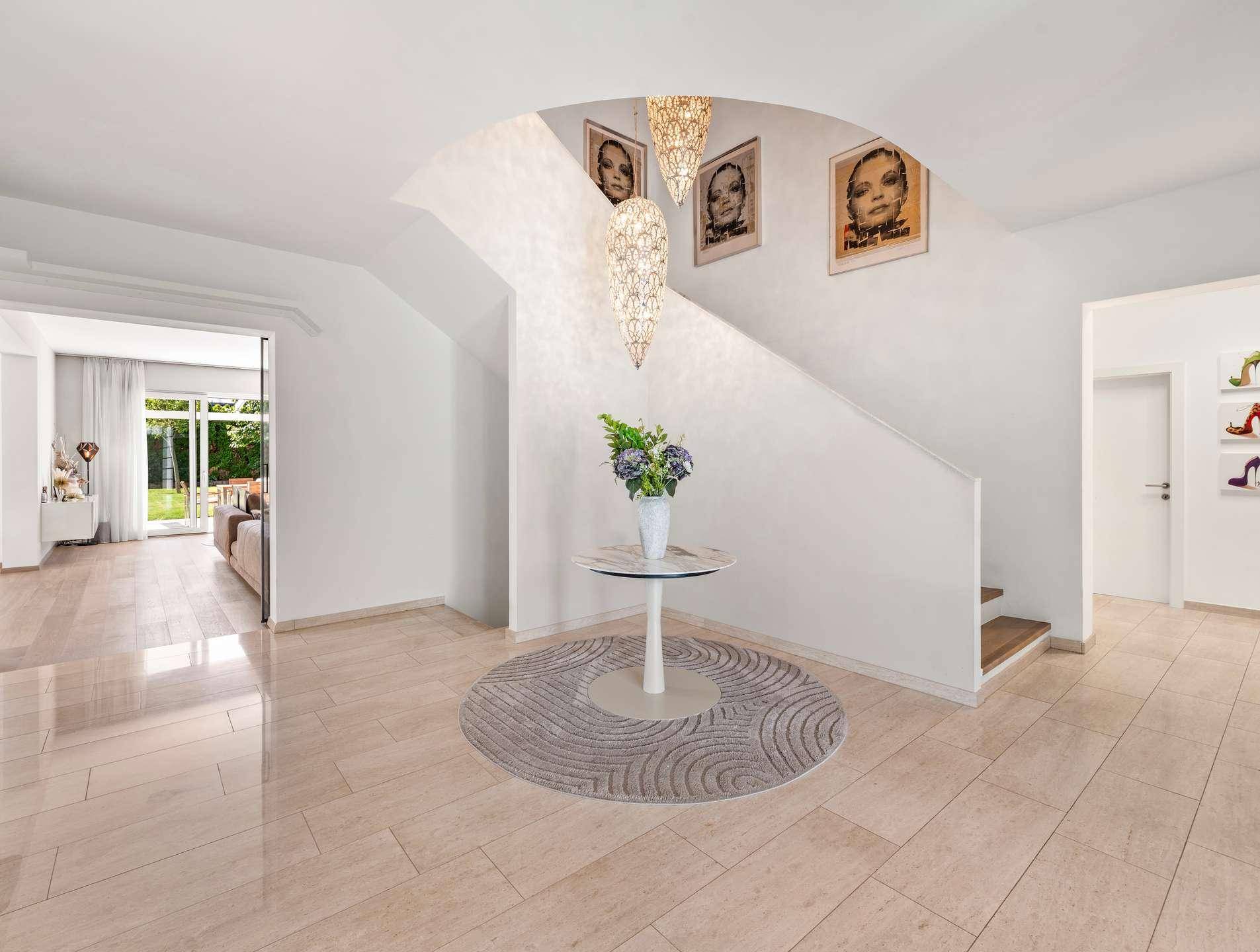Geräumiger Eingangsbereich mit hellem Fliesenboden, eleganter Treppe und dekorativem Beistelltisch.