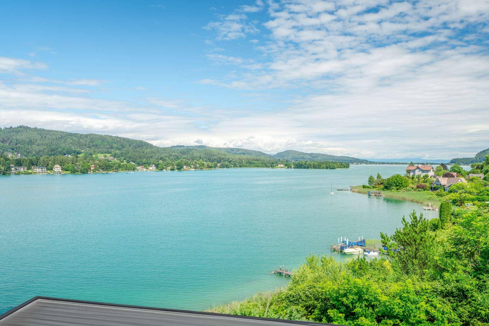 Panoramablick auf einen weiten, türkisfarbenen See, umgeben von grünen Hügeln und vereinzelten Häusern.