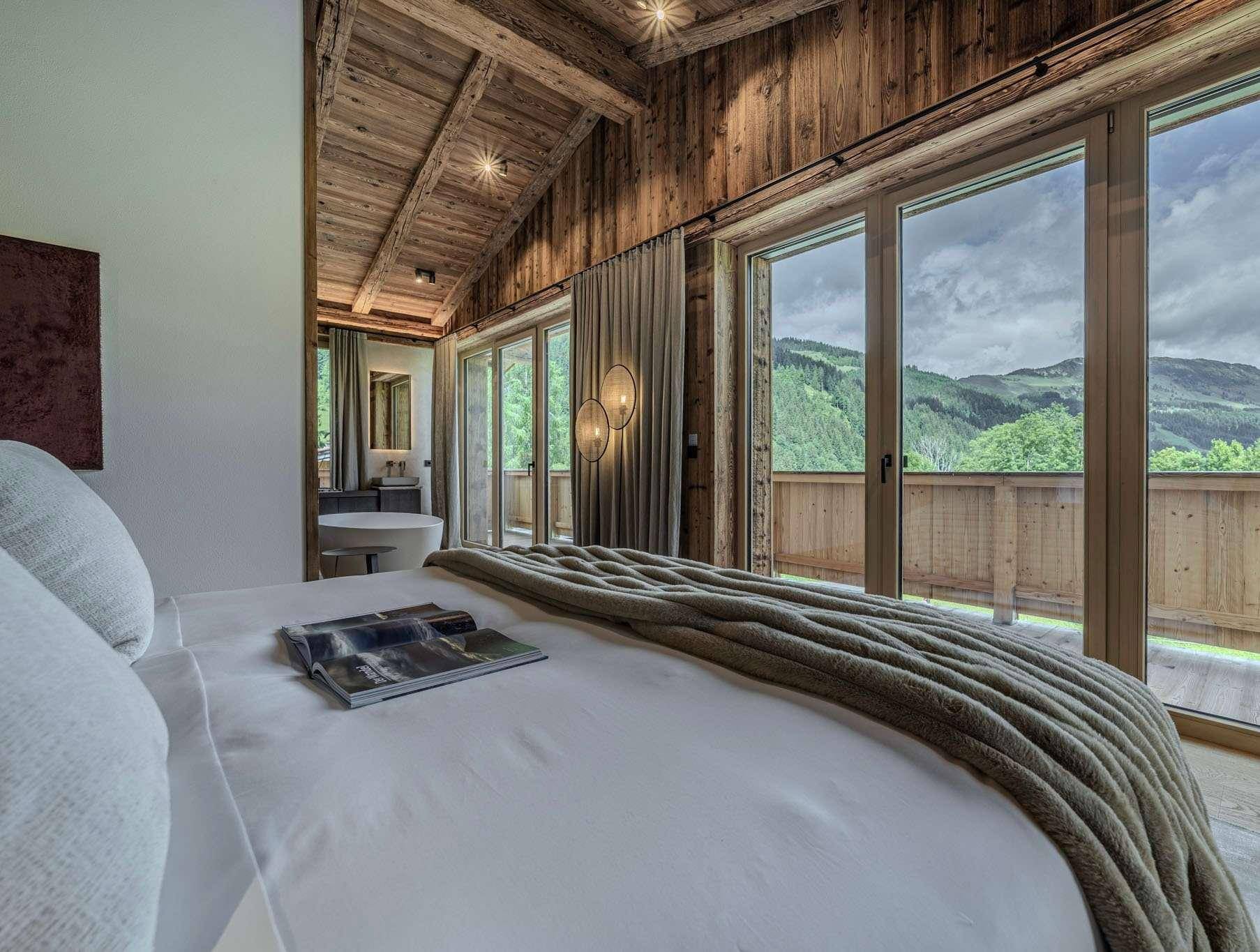 Schlafzimmer mit Holzwänden, großen Fenstern und Zugang zum Balkon mit Bergblick.